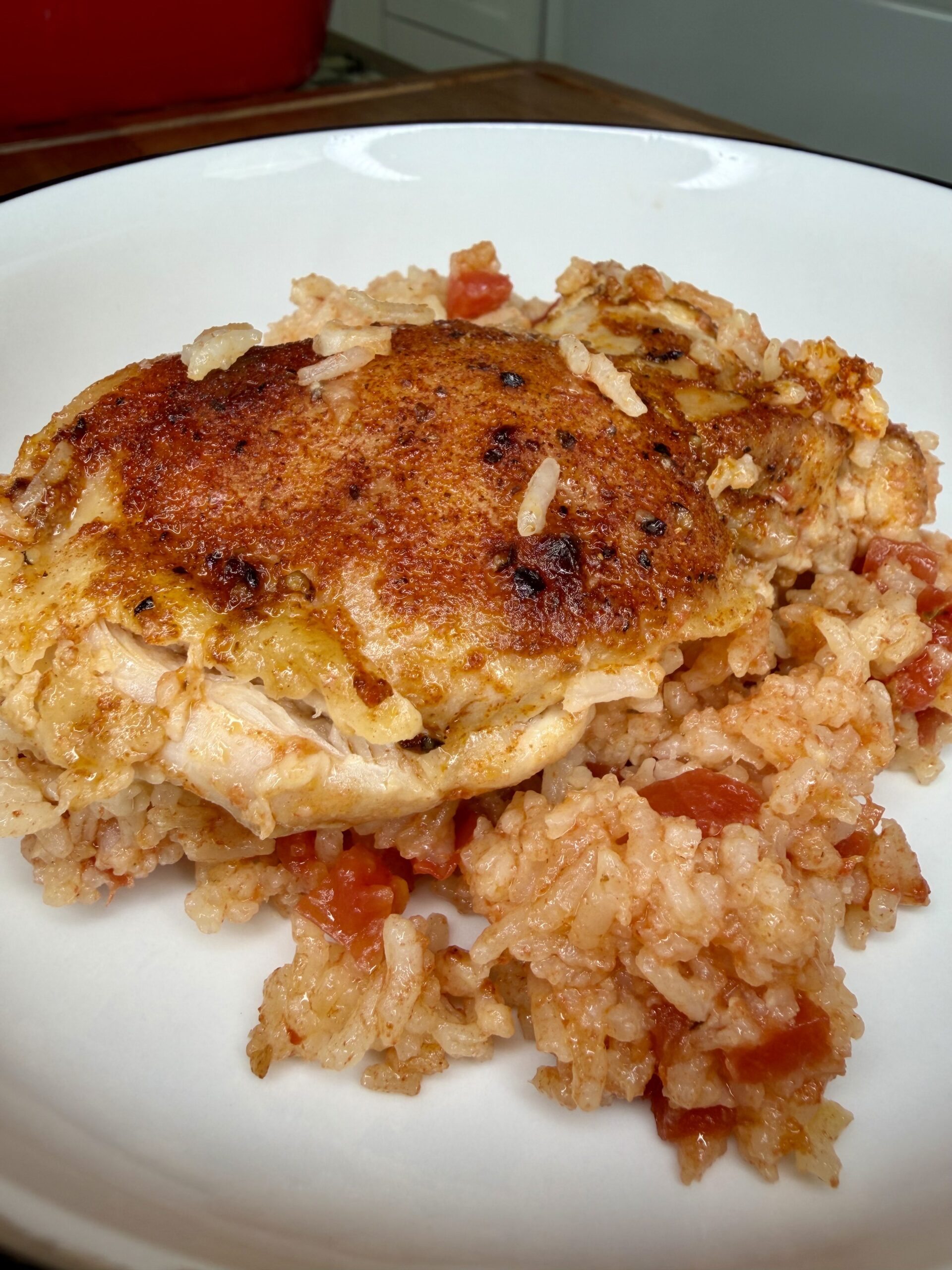 A close-up of a baked, seasoned chicken breast served on a bed of tomato rice, presented in a white bowl.
