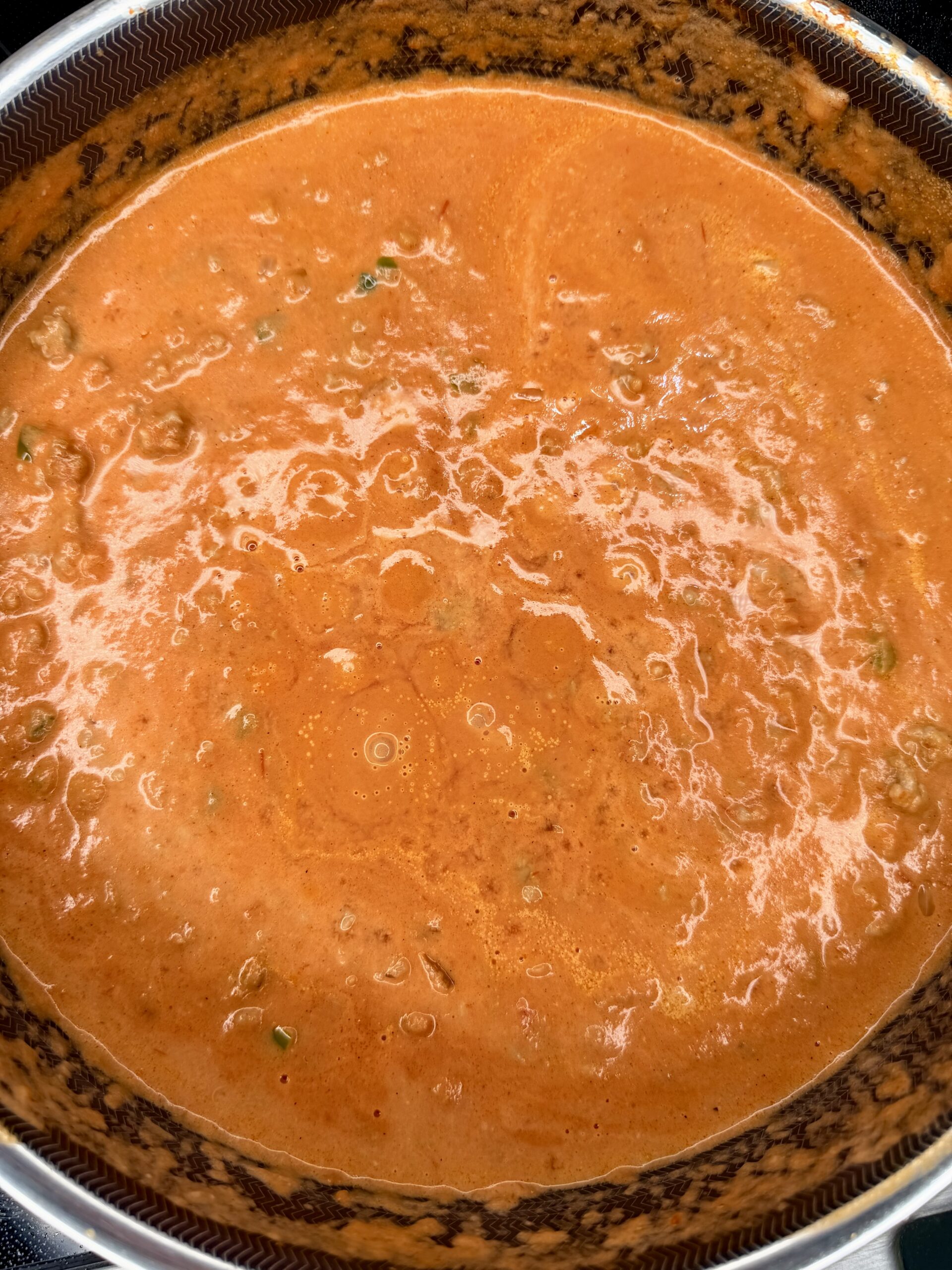 A close-up of a pot filled with thick, creamy orange-red tomato sauce, with small bubbles and herbs visible on the surface.