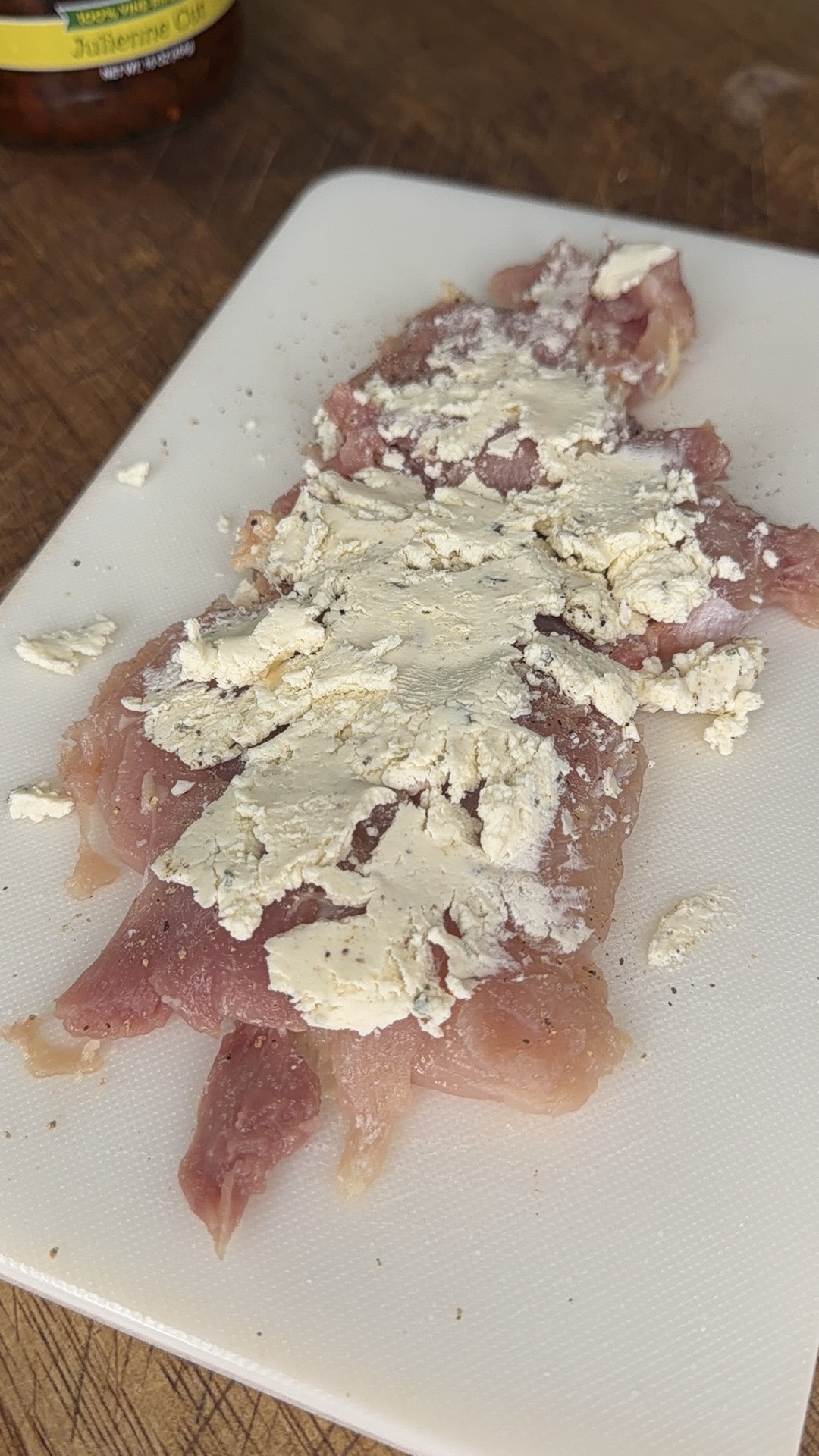 Raw pieces of chicken on a white cutting board, topped with a layer of powdered seasoning, on a wooden surface.