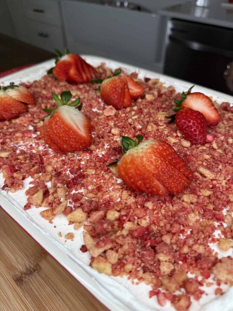 A close-up of a dessert topped with crumbled cookie pieces and whole fresh strawberries, set on a wooden surface in a kitchen—perfect for The Ultimate Easter Menu (Mediterranean & American).