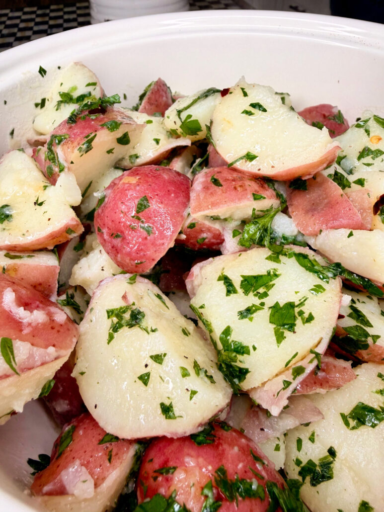 A close-up of a bowl filled with sliced red potatoes mixed with chopped fresh parsley and onions, creating a colorful and fresh-looking potato salad.