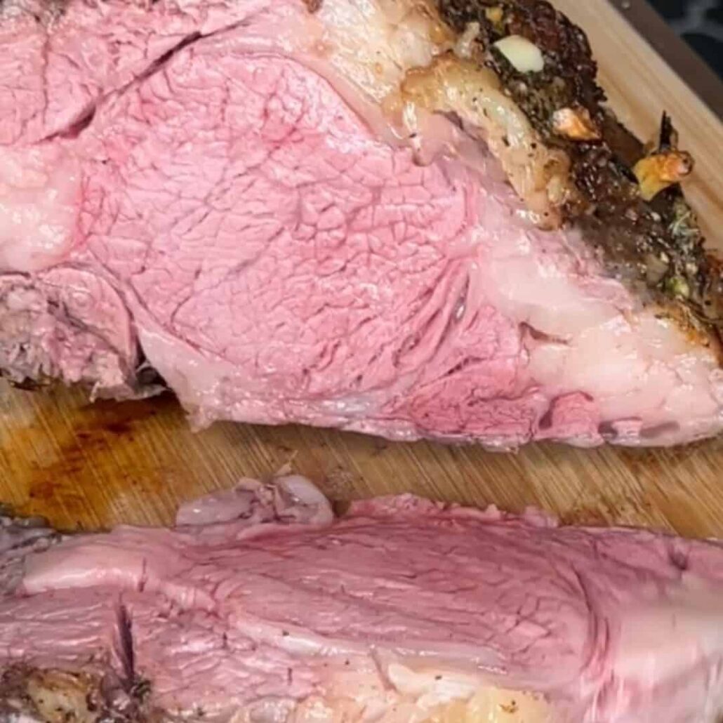 A close-up of a sliced piece of medium-rare roast beef on a wooden cutting board, showing a pink, juicy interior and a seasoned, browned crust.