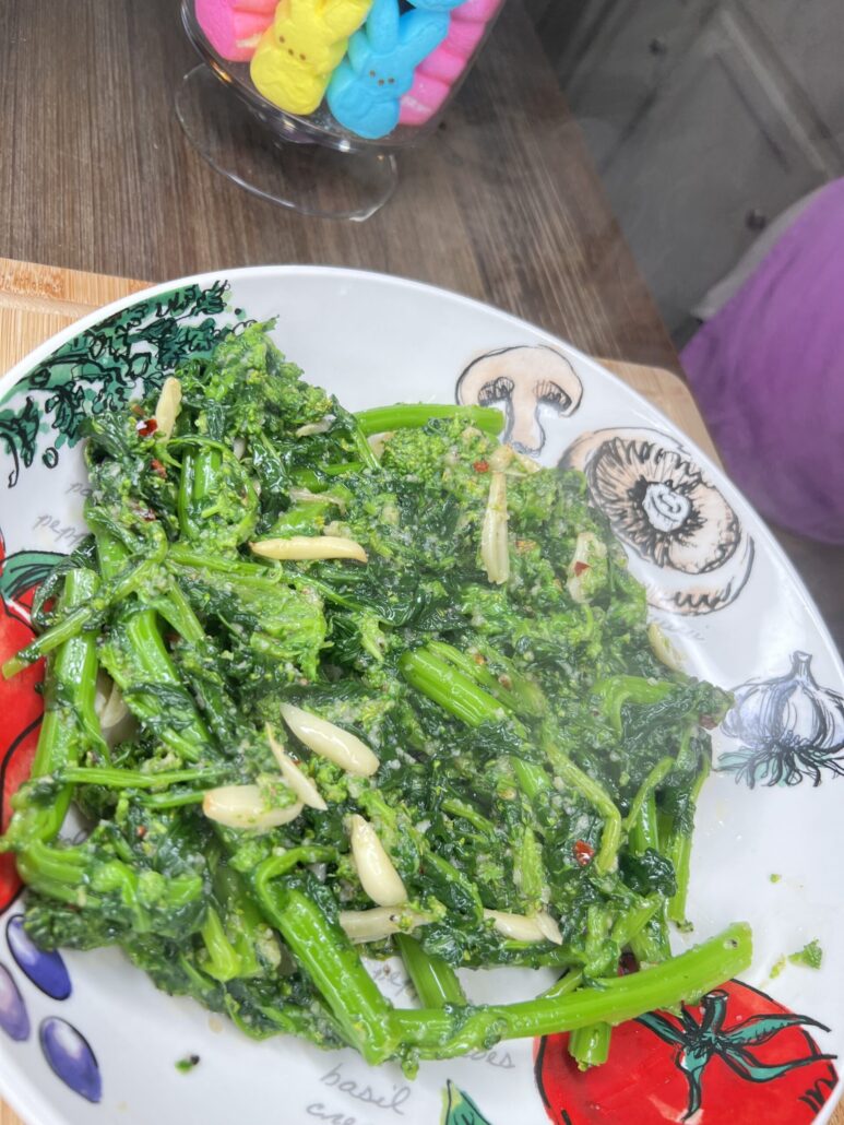 A plate of sautéed greens with garlic slices on a colorful vegetable-themed dish, with a jar of pastel-colored marshmallow bunny candies in the background.
