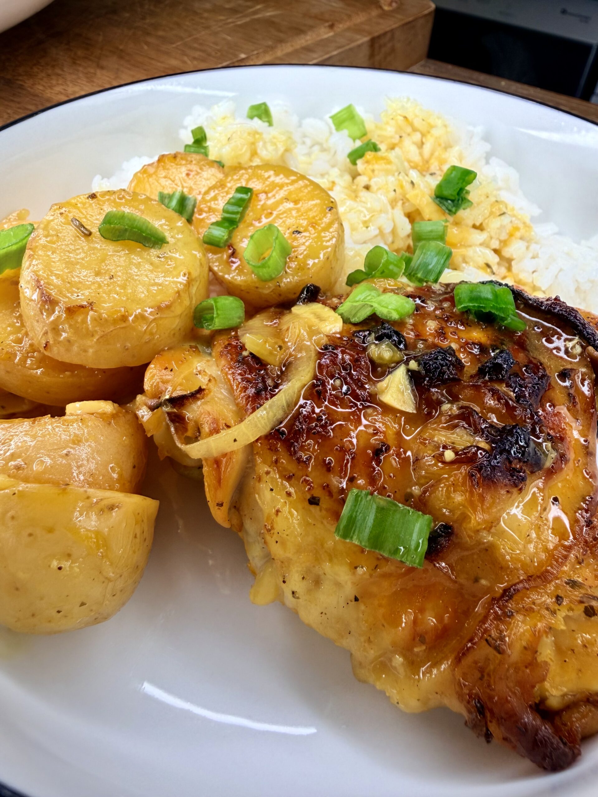 A plate featuring One-Pan Mojo Chicken & Potatoes, topped with green onions and golden potatoes in sauce, served alongside white rice with fluffy scrambled eggs.