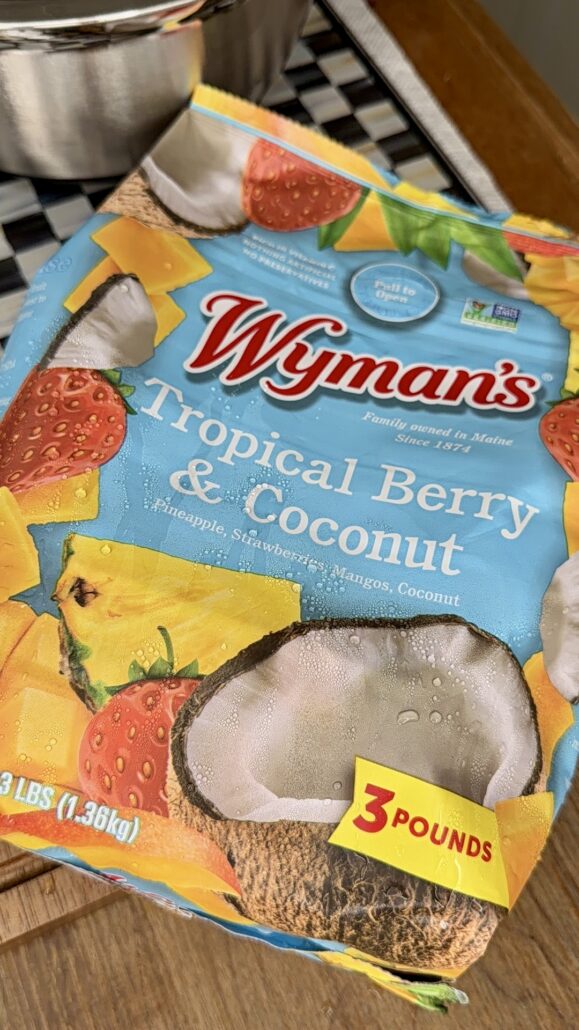 A bag of Wymans Tropical Berry & Coconut blend, showing images of pineapple, strawberries, mango, and coconut. The label notes its a 3-pound bag with non-GMO ingredients.