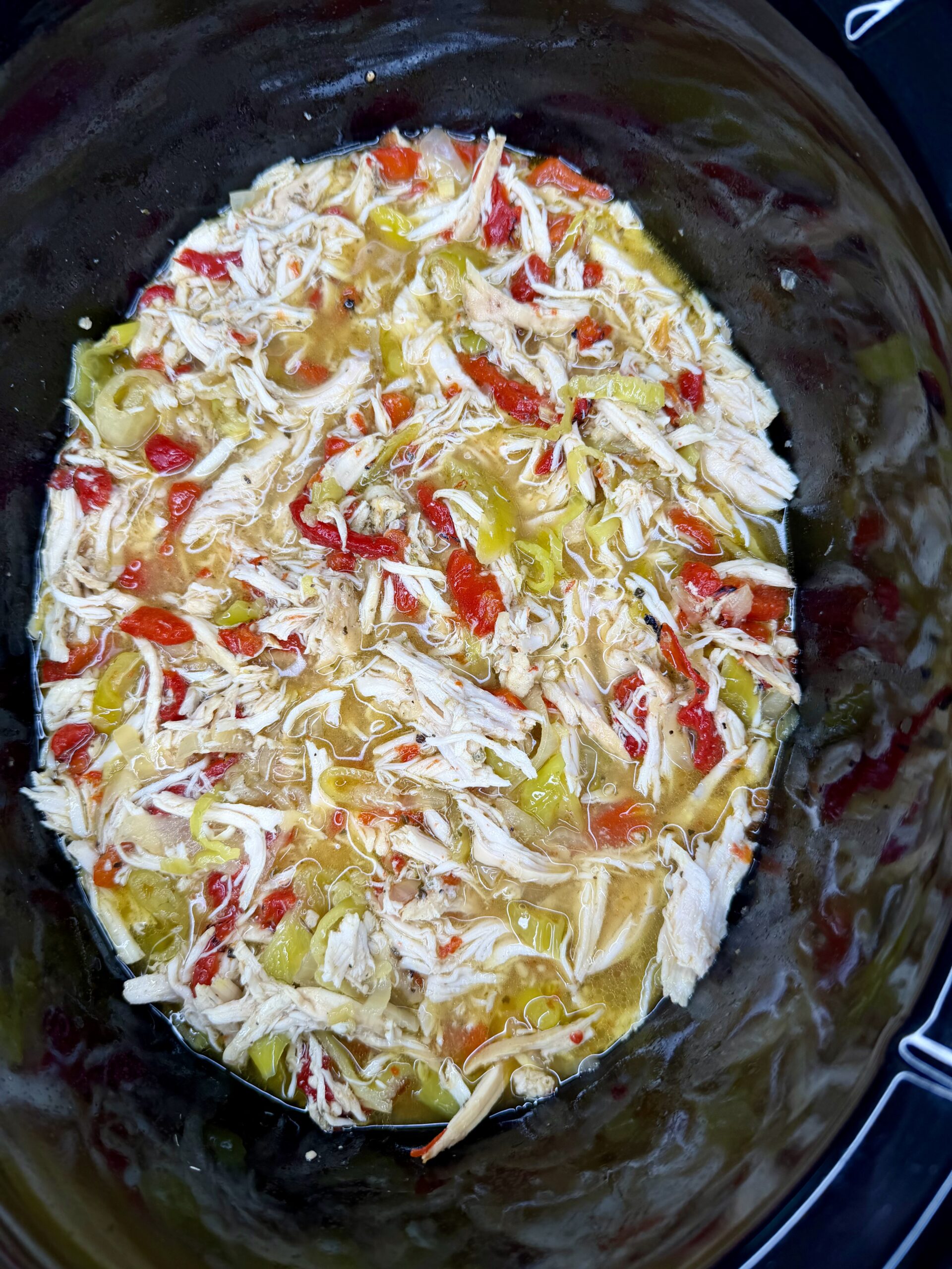 Easy Crockpot Chicken Philly Cheesesteak: Shredded chicken mixed with chopped red and green peppers in a slow cooker, surrounded by savory broth.