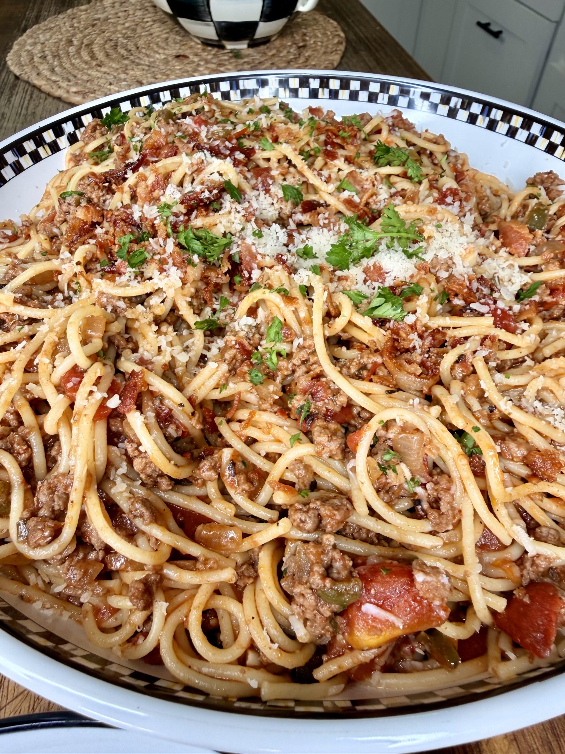 A close-up of a large bowl filled with spaghetti topped with ground meat, tomato sauce, chopped herbs, and grated cheese, set on a wooden table.