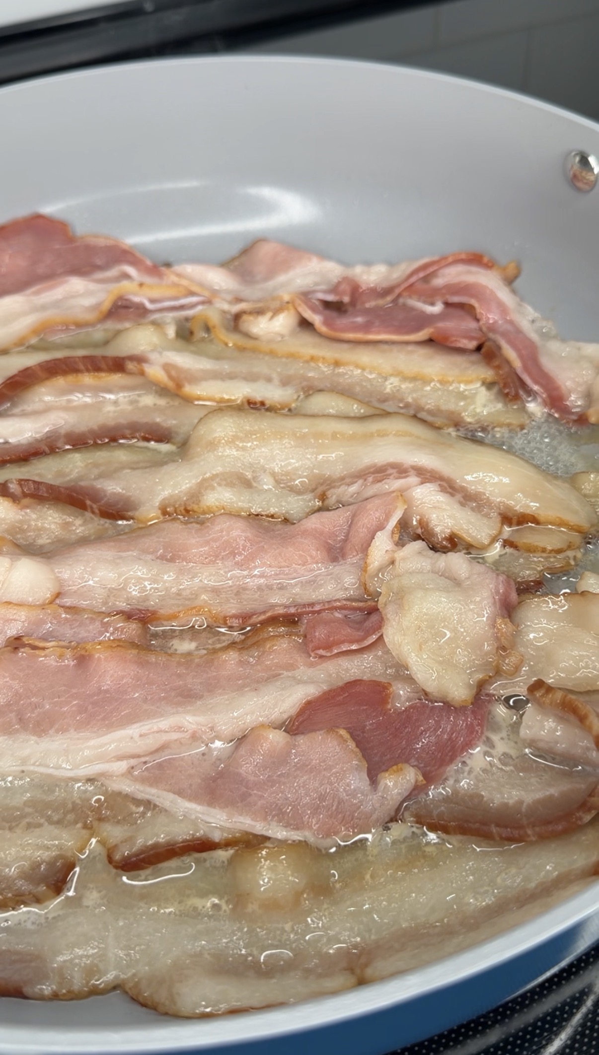 Several strips of bacon sizzling and cooking in a pan, with visible bubbling fat and edges starting to crisp.