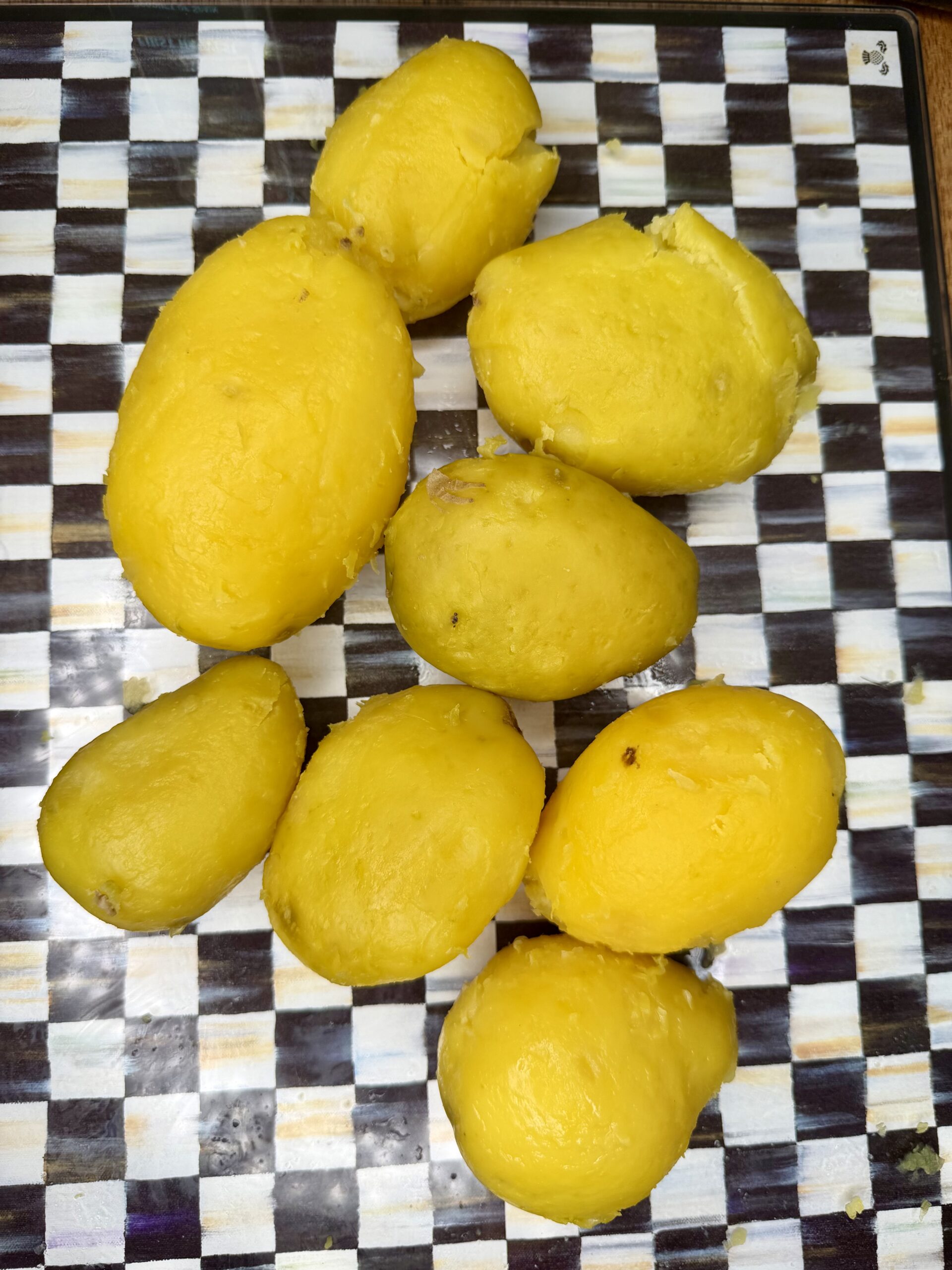 Peeled, boiled yellow potatoes are placed on a checkered surface with alternating black, white, and gray squares.