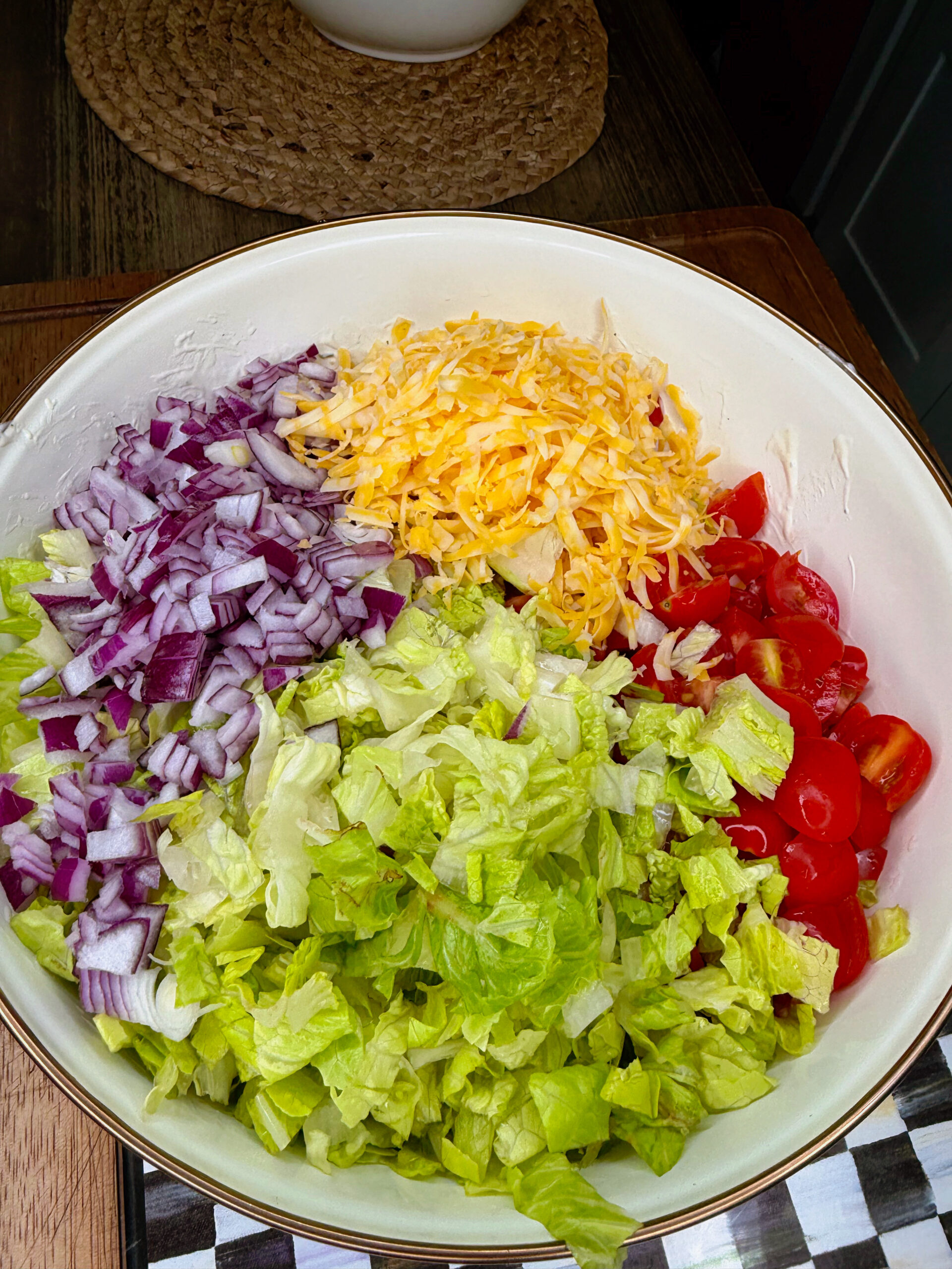 A large bowl filled with chopped red onions, shredded cheddar cheese, halved cherry tomatoes, and chopped romaine lettuce, arranged in separate sections.