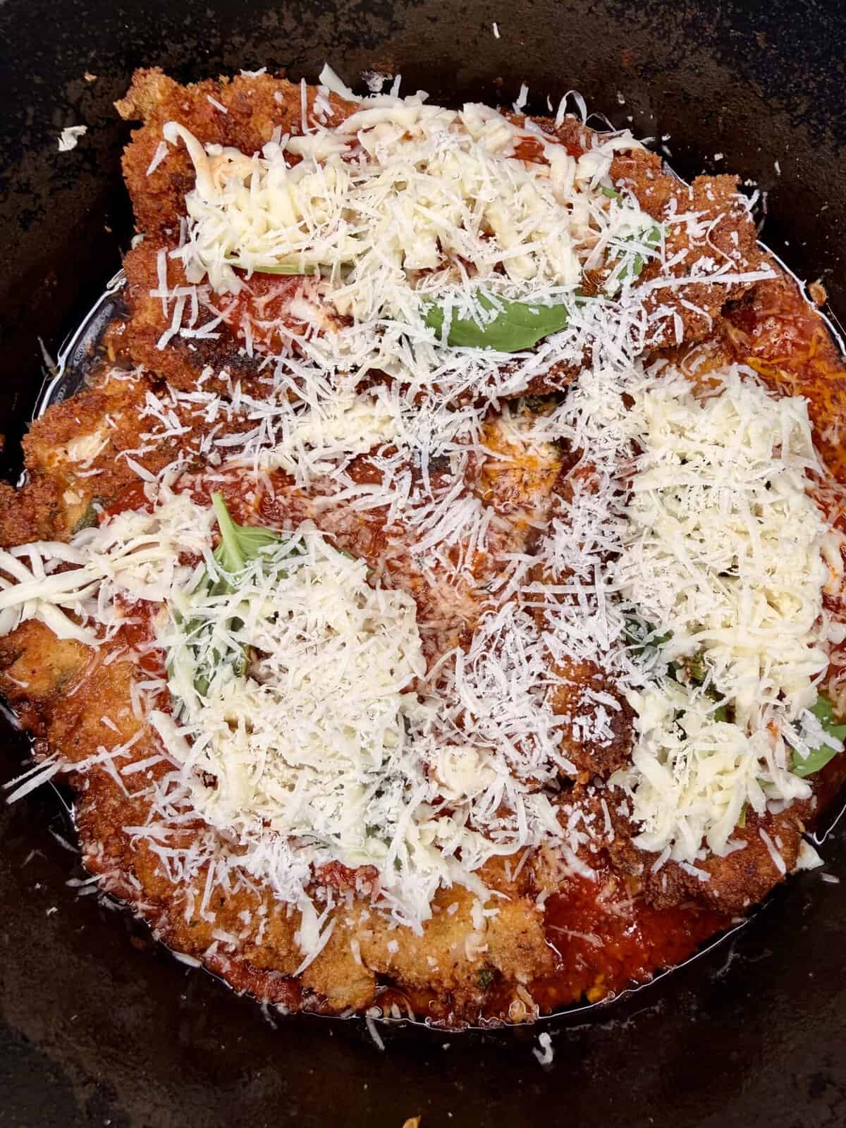 A close-up of chicken parmesan in a pan, topped with tomato sauce, melted mozzarella, grated parmesan cheese, and fresh basil leaves.