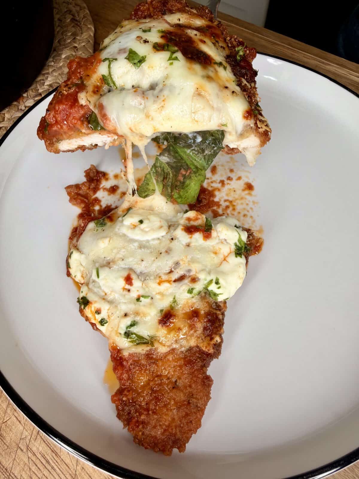 A breaded chicken cutlet topped with melted mozzarella cheese and tomato sauce is being lifted from a plate, revealing a layer of fresh spinach and ricotta cheese underneath.