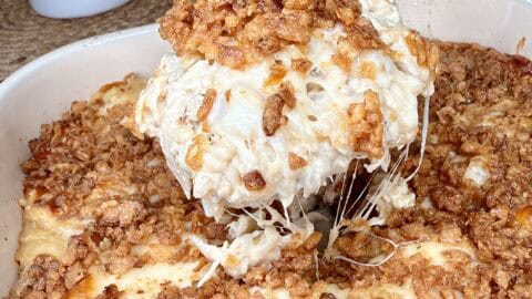 A spatula lifts a cheesy, golden-brown casserole topped with crispy fried onions from a baking dish in a bright kitchen.
