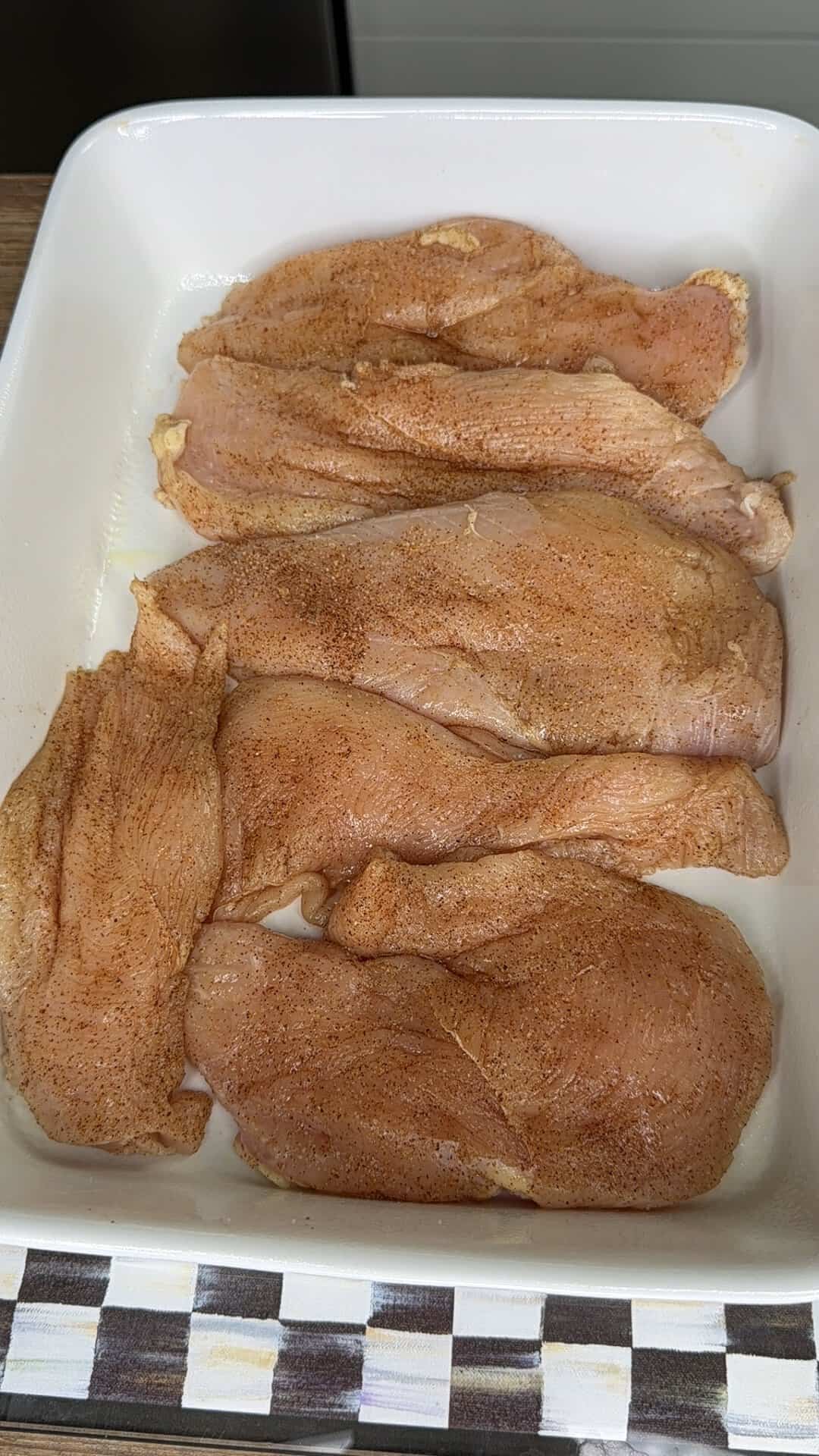 Raw, seasoned chicken breast fillets arranged in a single layer in a white baking dish, ready to be cooked.