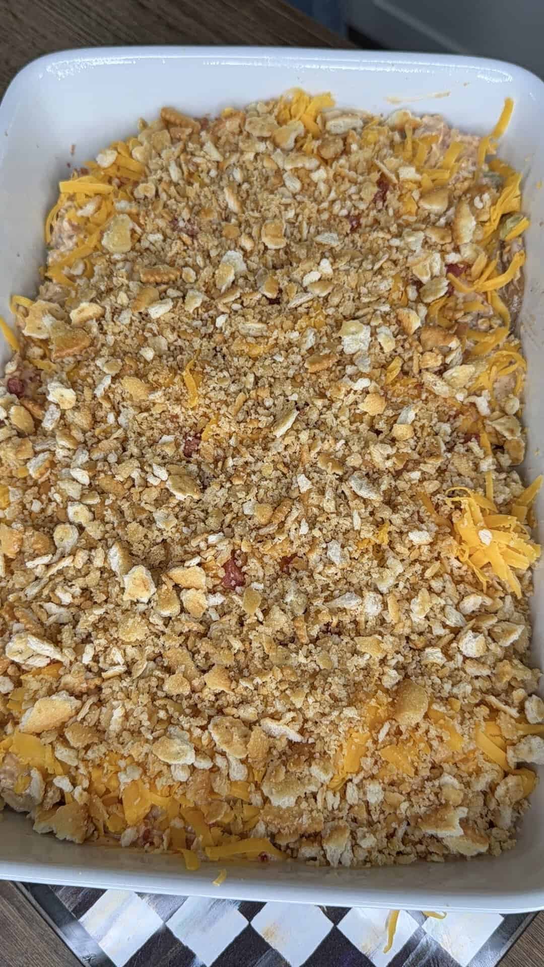 A casserole dish filled with a baked mixture topped with shredded cheese and a golden breadcrumb or cracker crumb topping, sitting on a table.