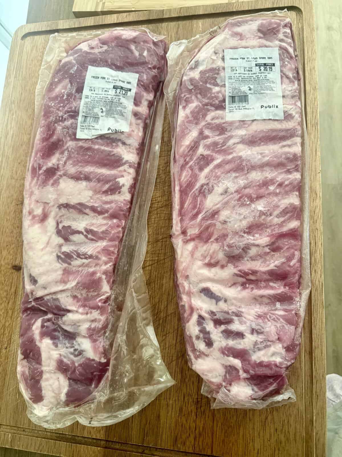 Two packages of raw pork ribs in clear vacuum-sealed plastic, labeled with store and weight information, are placed on a wooden surface.