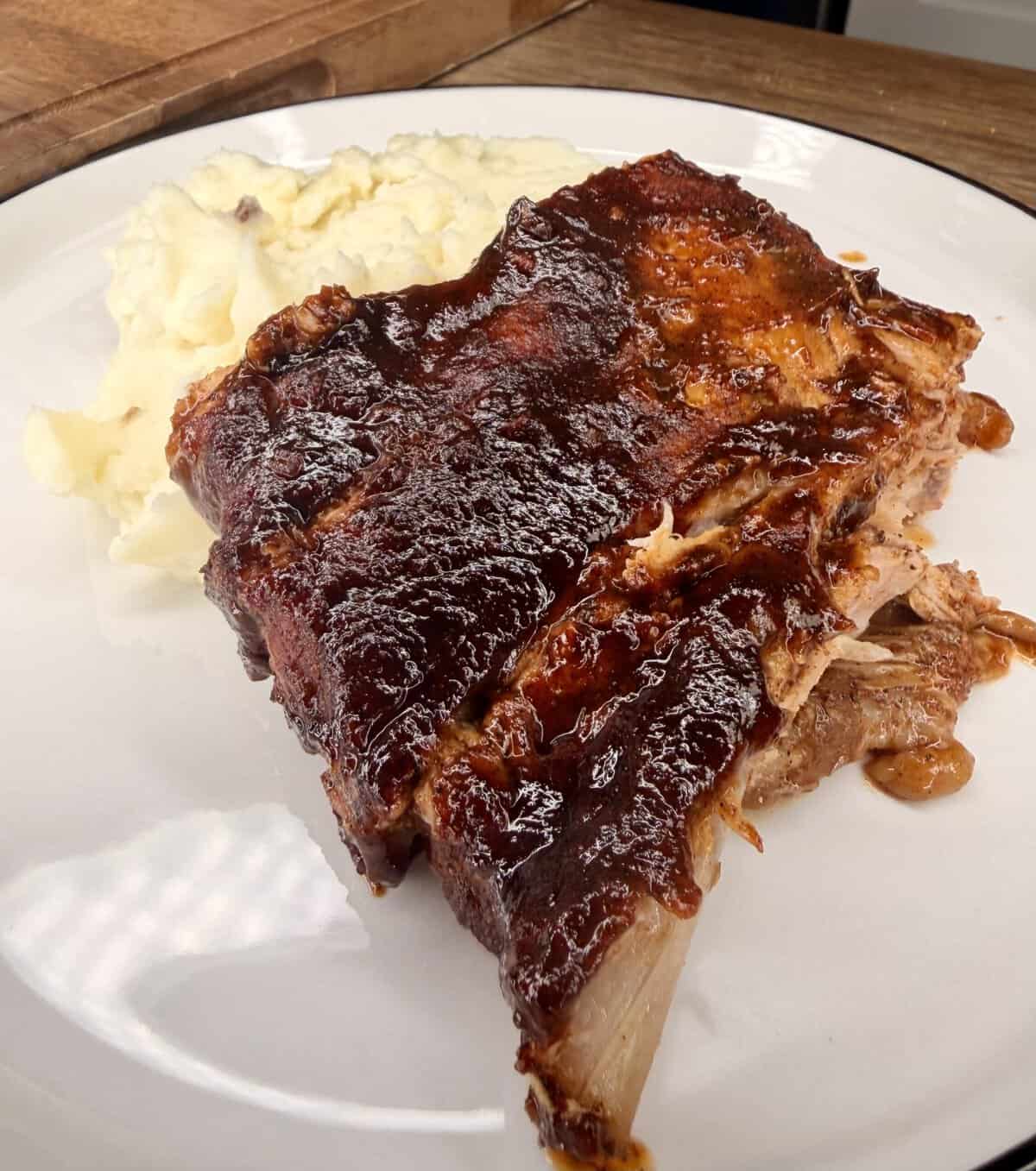 A plate with barbecued pork ribs covered in a shiny sauce, served alongside a generous portion of creamy mashed potatoes.