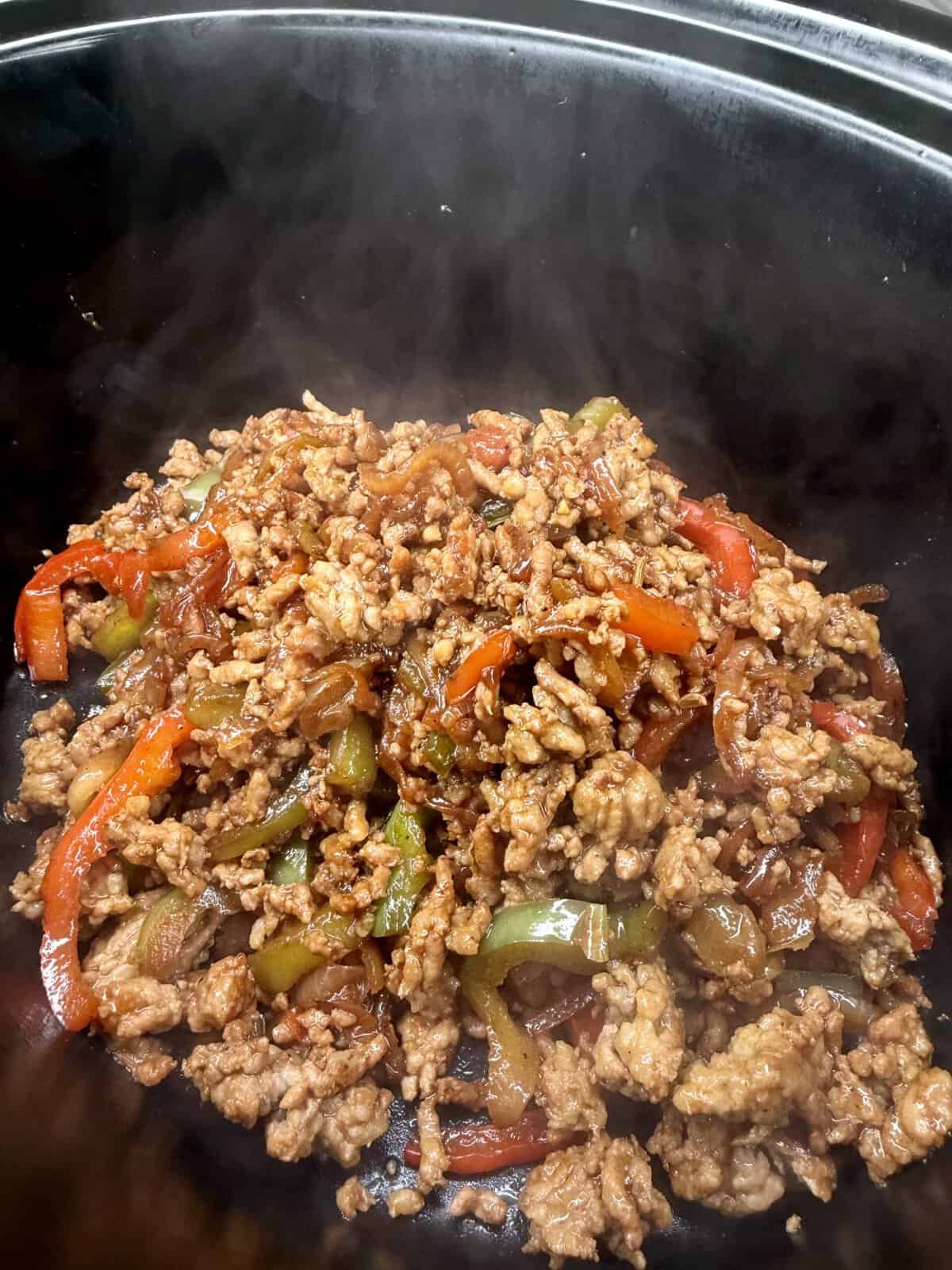 Ground meat cooked with sliced red and green bell peppers and onions in a dark sauce, served in a black dish with visible steam rising from the food.