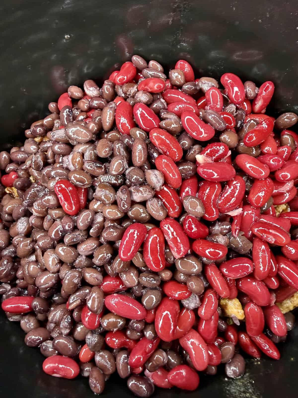 A close-up of shiny red kidney beans and dark black beans mixed together in a pot or container.