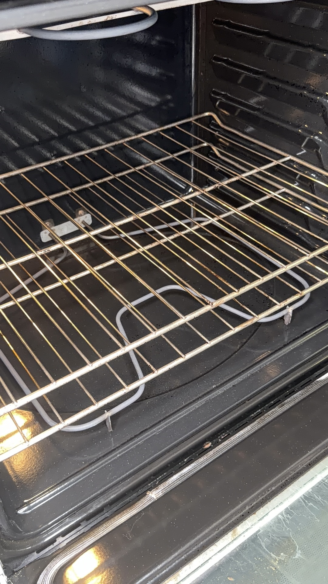 Open oven with two metal racks inside, heating element visible at the bottom, and oven lights on, illuminating the interior.