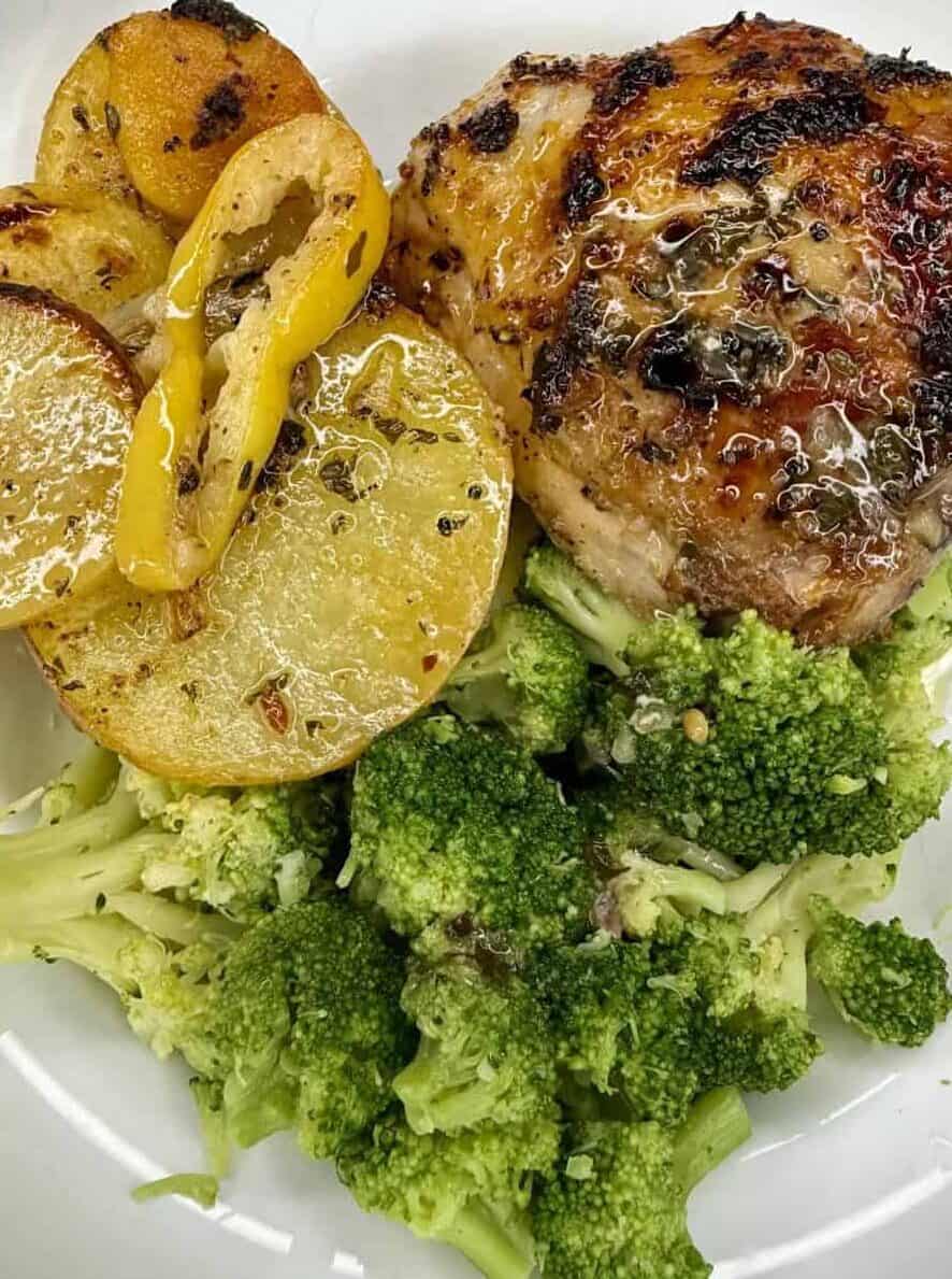 A plate with roasted chicken thigh, sliced roasted potatoes with yellow bell pepper, and steamed broccoli.
