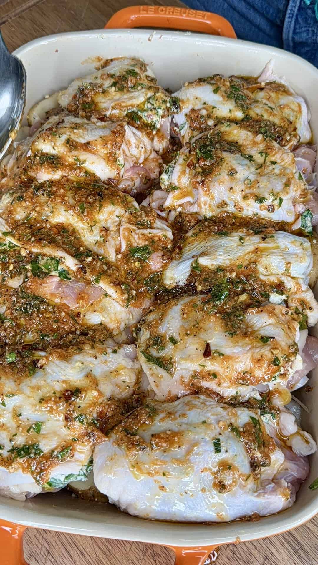 Raw chicken pieces arranged in a baking dish, covered with a marinade made of herbs, spices, and oil, ready to be cooked.