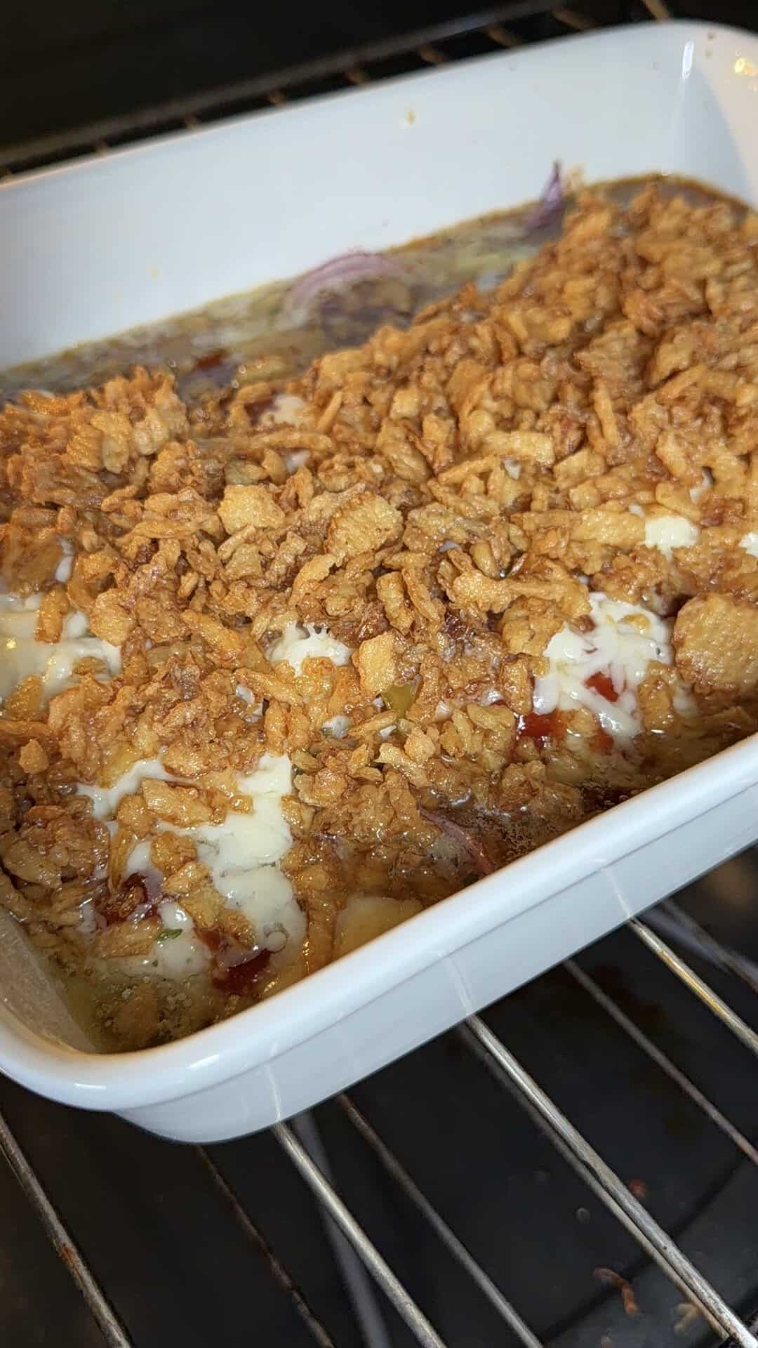 A casserole dish in an oven filled with a baked casserole topped with crispy fried onions and melted cheese.