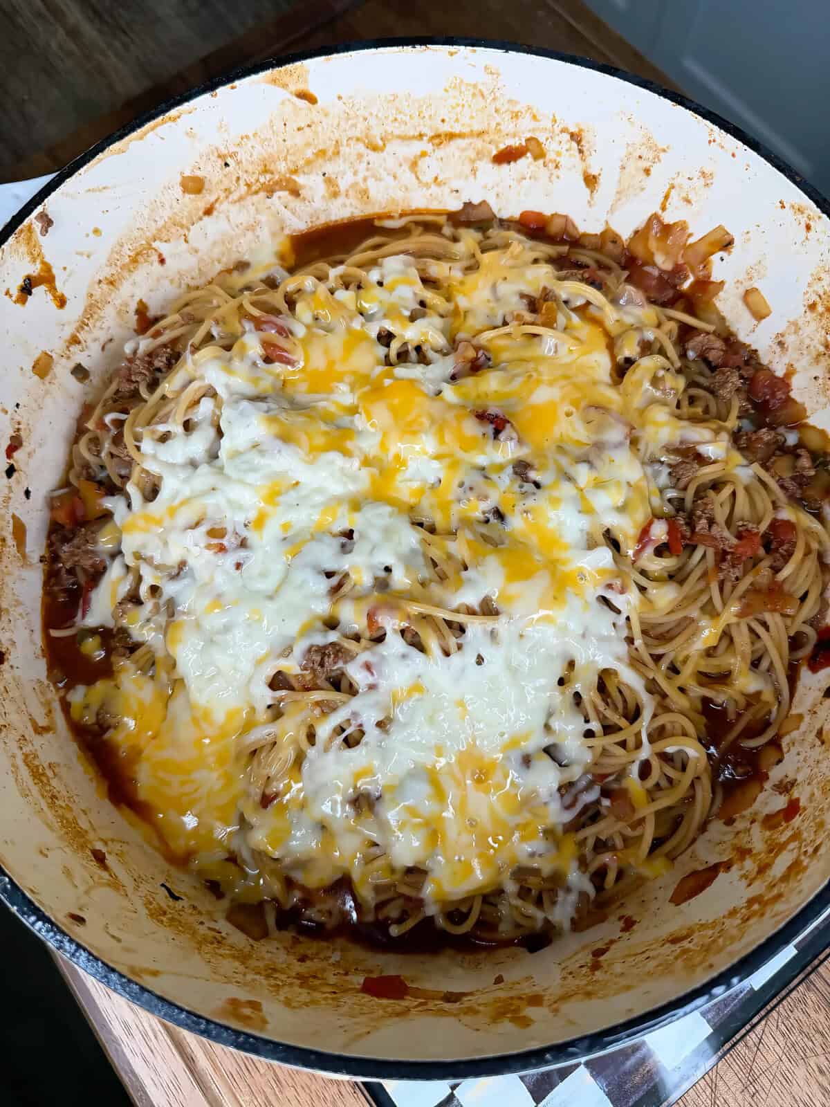 A large pot of spaghetti with ground meat, tomato sauce, and melted shredded cheese on top, mixed together and ready to serve.