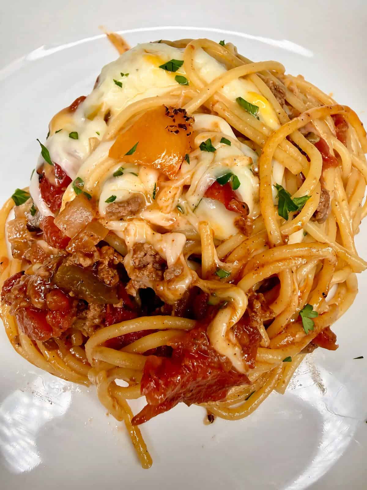 A close-up of baked spaghetti with ground meat, melted cheese, tomato sauce, and herbs on a white plate.
