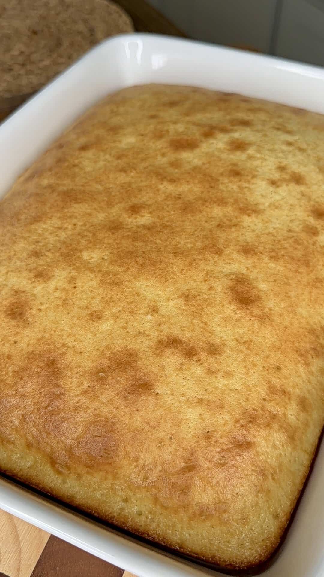 A golden-brown, rectangular sheet cake in a white baking dish, freshly baked and resting on a wooden surface.