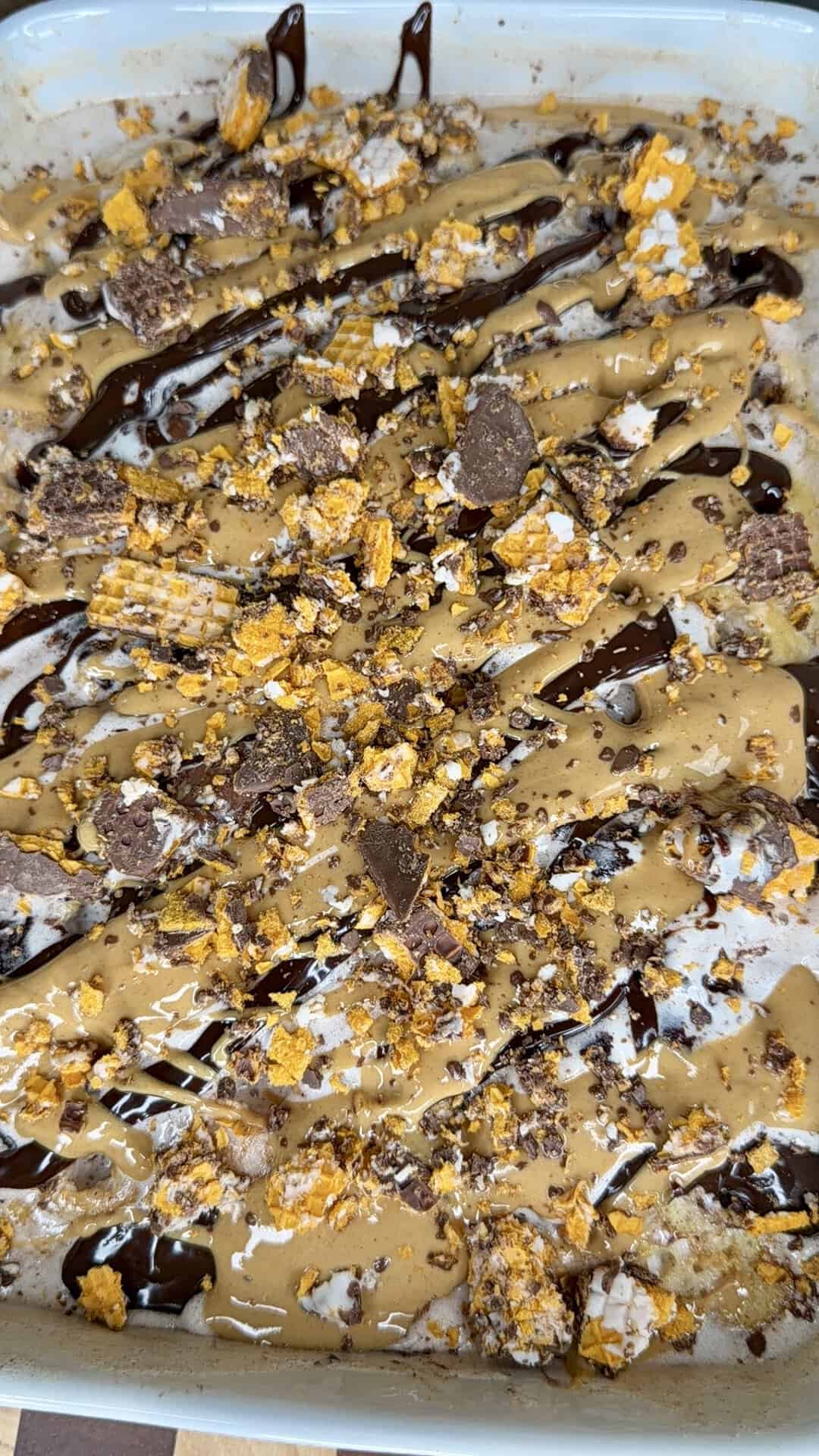 A close-up of a dessert topped with drizzled chocolate, caramel, and crushed candy pieces in a rectangular dish.