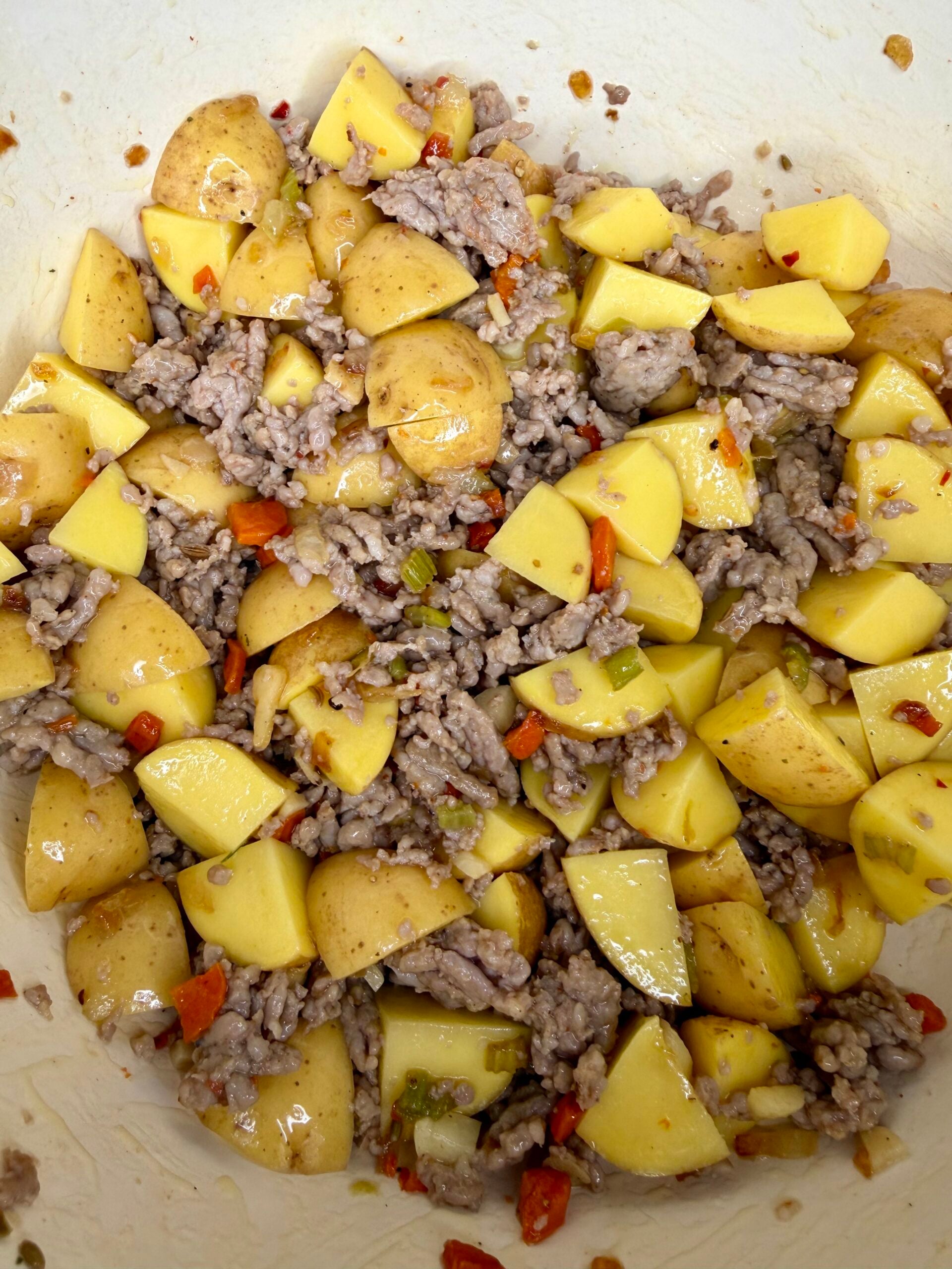 Chopped yellow potatoes, cooked ground meat, and diced red and green peppers mixed together in a white bowl.