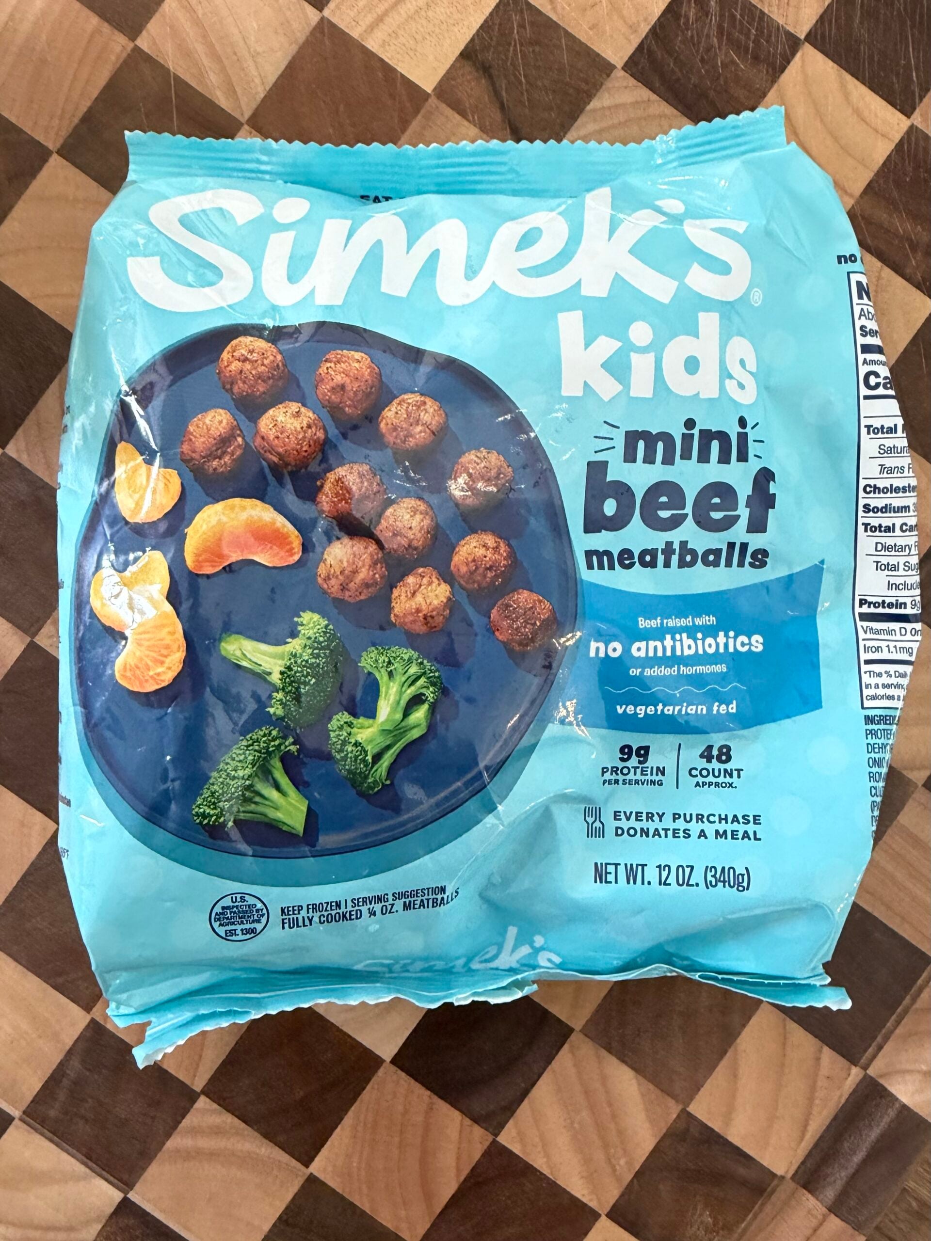A blue bag of Simeks Kids mini beef meatballs, showing a plate with meatballs, broccoli, and orange slices. The packaging highlights no antibiotics, 9g protein, and 48 meatballs per bag.
