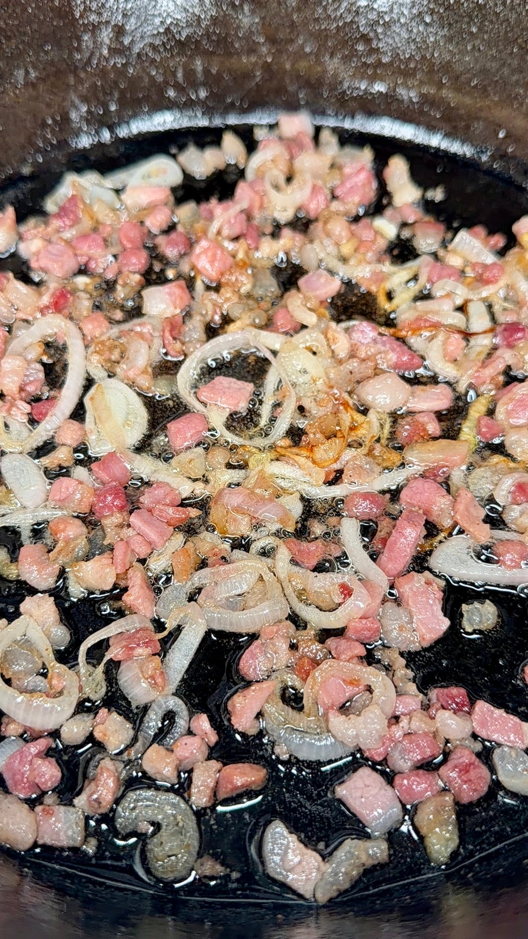 Chopped bacon and sliced shallots sizzling and browning in a pan with oil.
