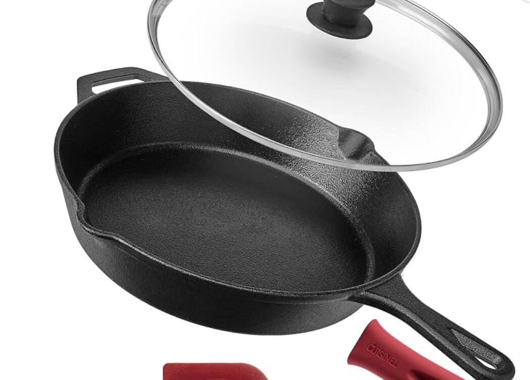 A black cast iron skillet with a glass lid, a red silicone handle cover, and a red scraper tool are shown on a white background.