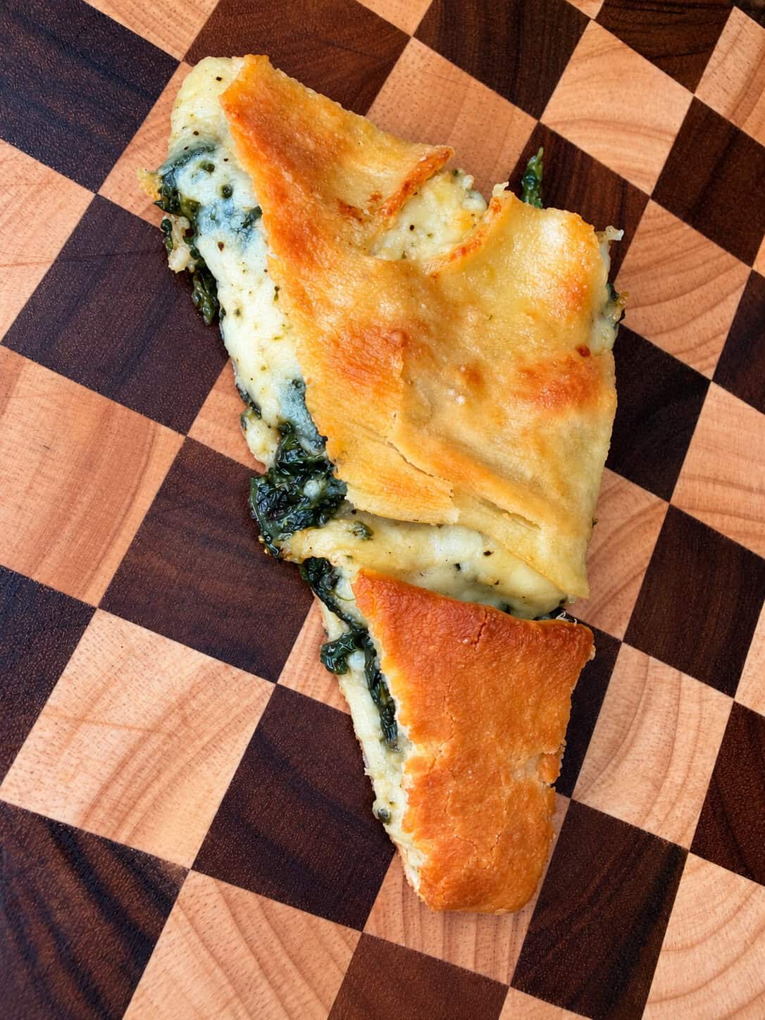 A slice of spinach and cheese calzone on a checkered wooden cutting board.