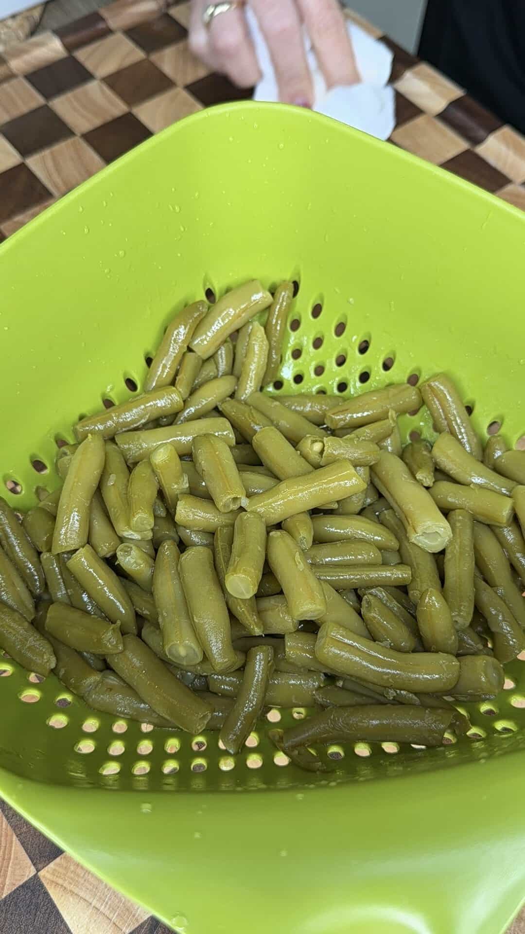 Cooked green beans in a lime green colander.