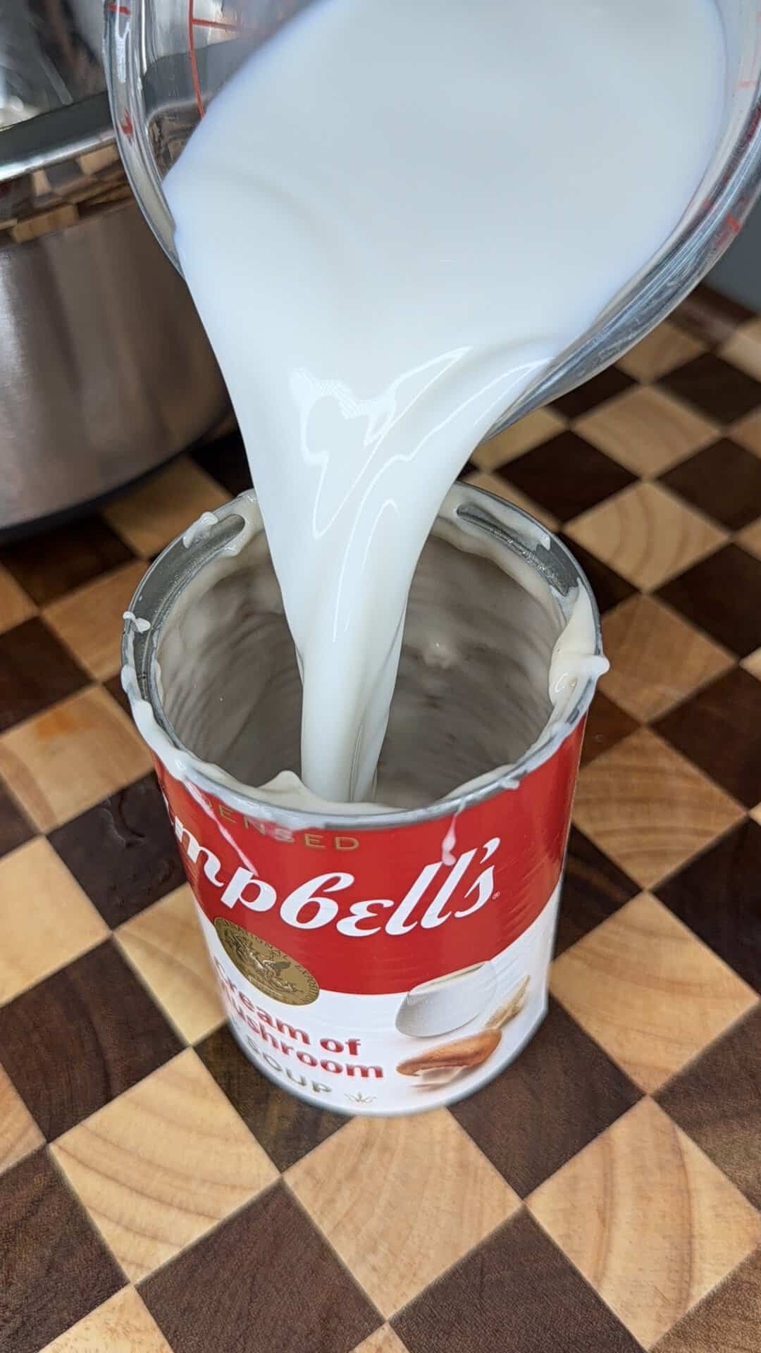 Milk being poured from a measuring cup into an open can of Campbells Cream of Mushroom soup.