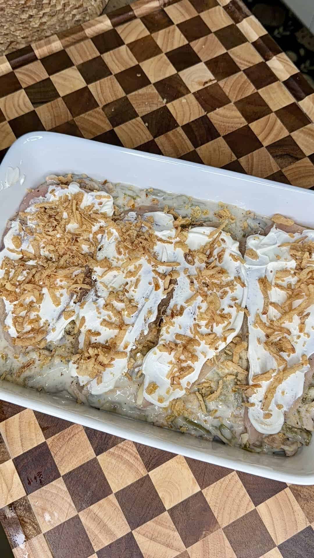 Casserole in a white rectangular dish, topped with slices of meat, dollops of sour cream, and crispy fried onions.