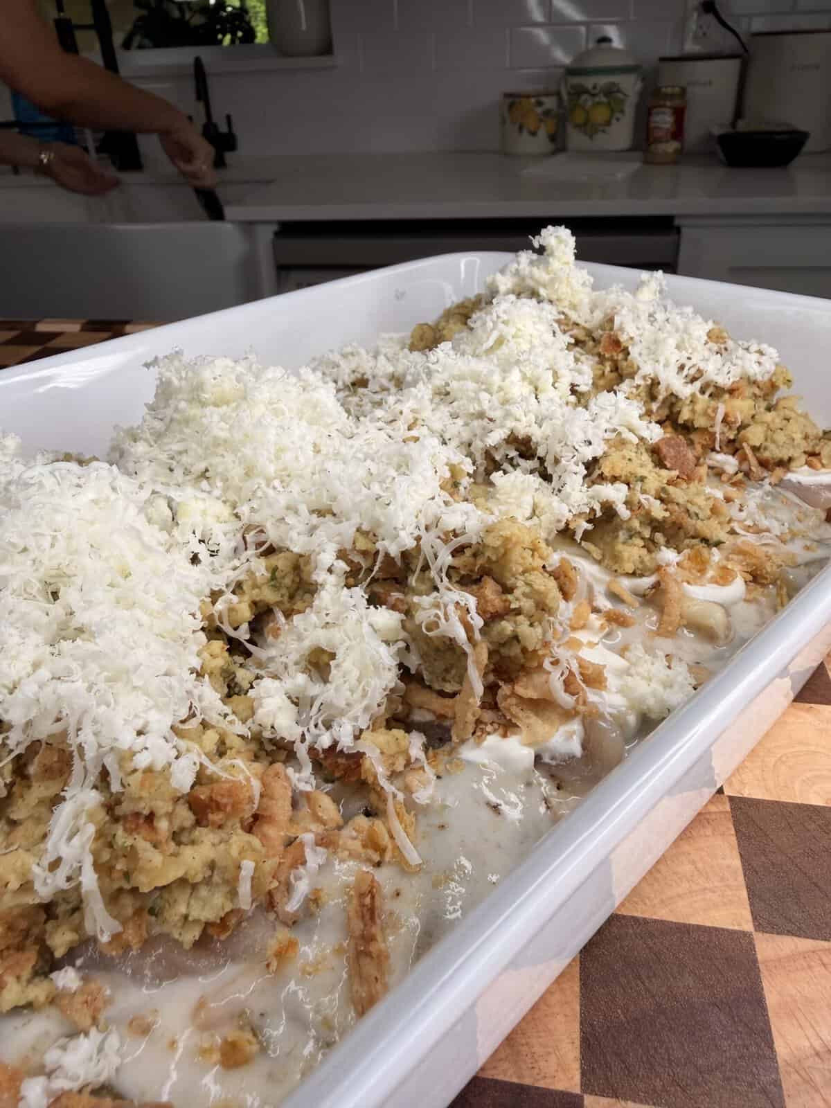 A rectangular casserole dish filled with layers of cream sauce, stuffing, and shredded cheese.