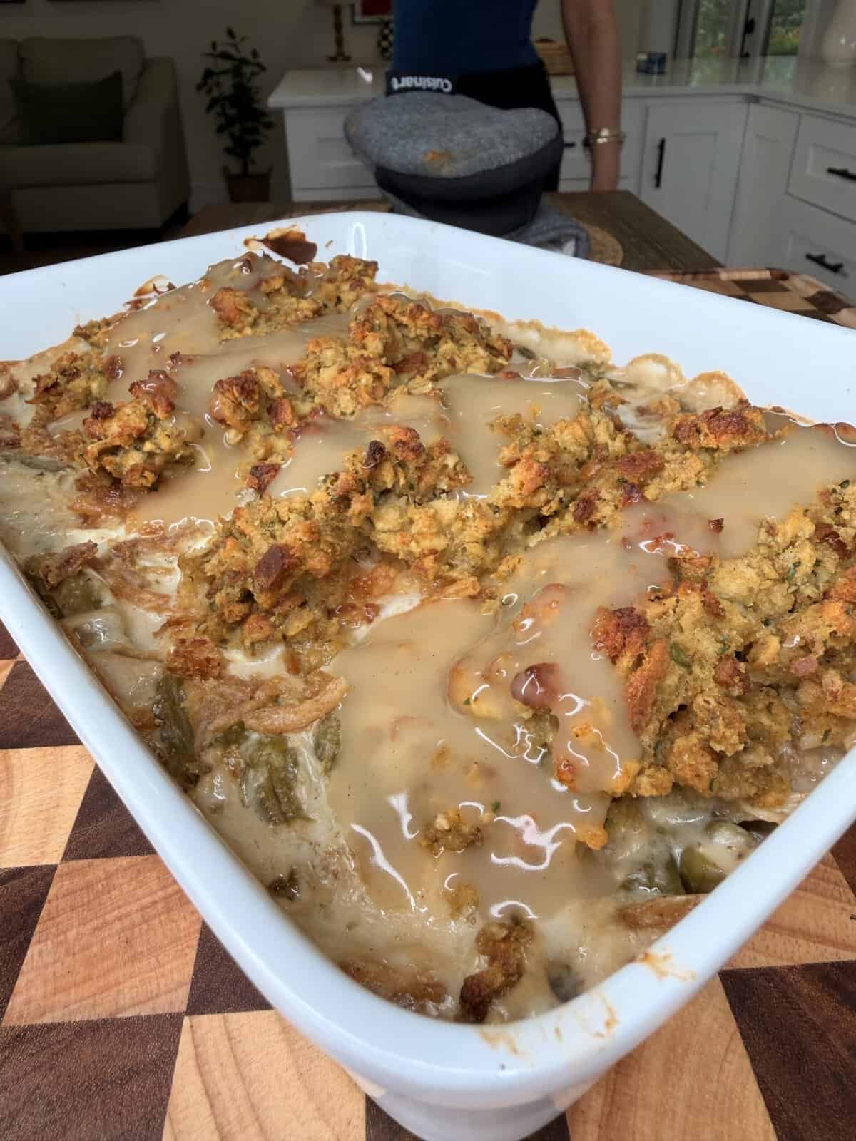 A rectangular baking dish filled with a green bean casserole topped with stuffing and drizzled with gravy.