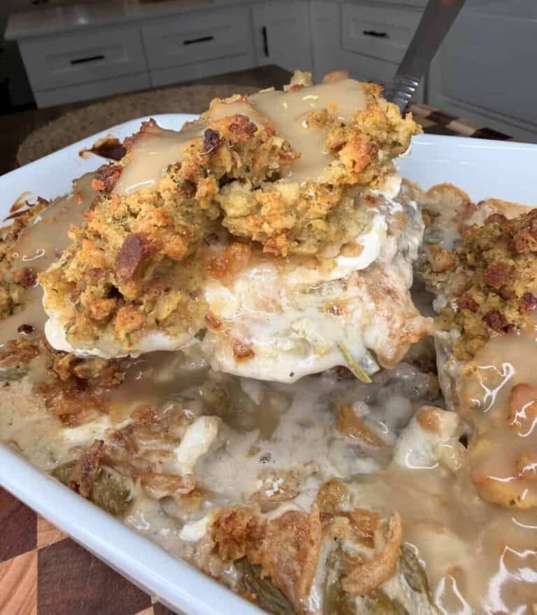 A serving spoon lifts a portion of creamy green bean casserole topped with stuffing and gravy from a baking dish.