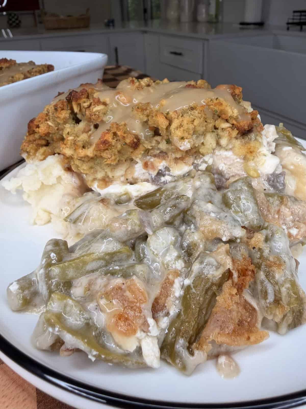 A dinner plate with a serving of mashed potatoes, stuffing topped with gravy, and creamy green bean casserole.