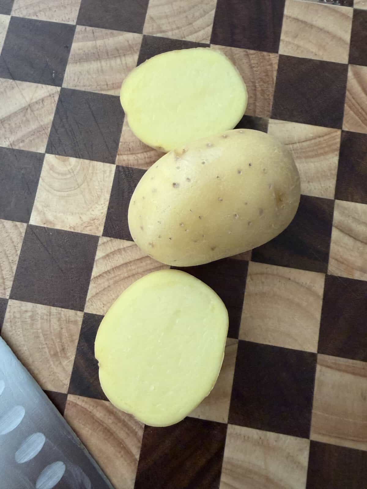 One whole potato and two potato slices arranged on a checkered wooden cutting board.