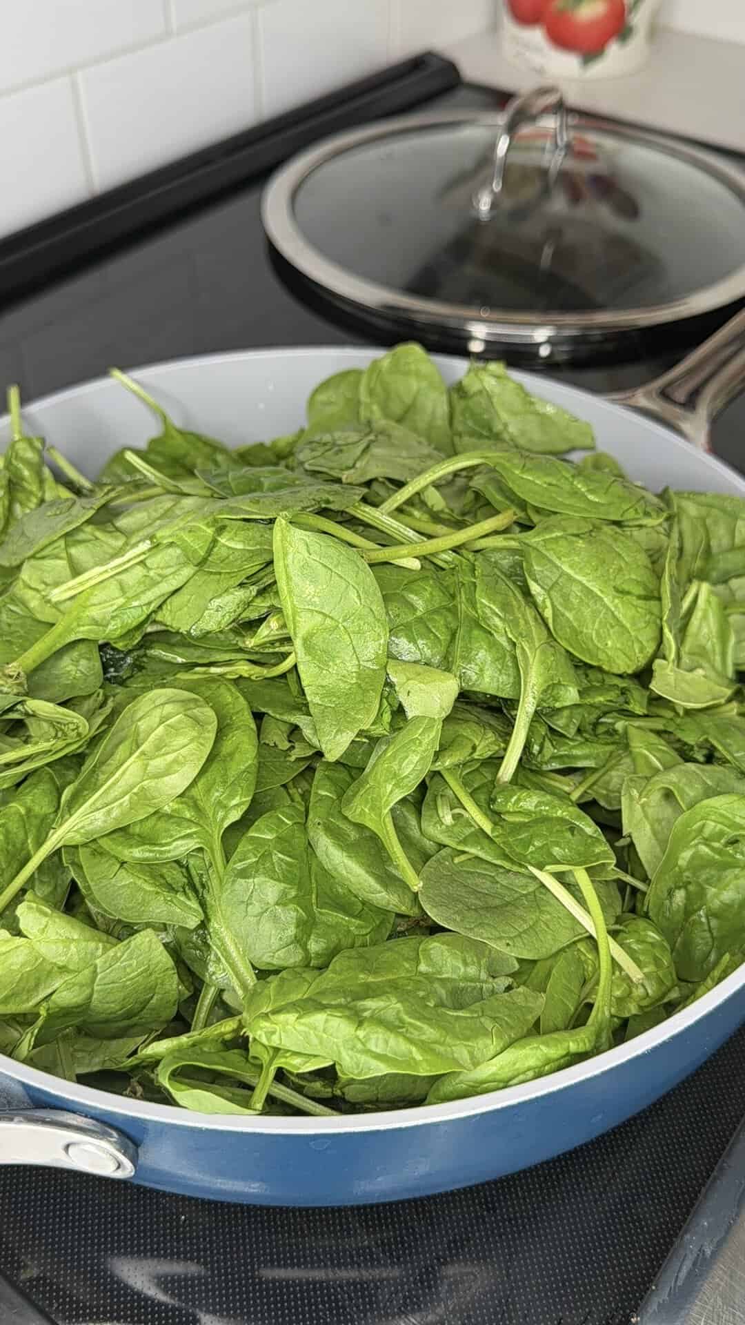 Fresh spinach leaves piled high in a blue cooking pan on a stovetop.