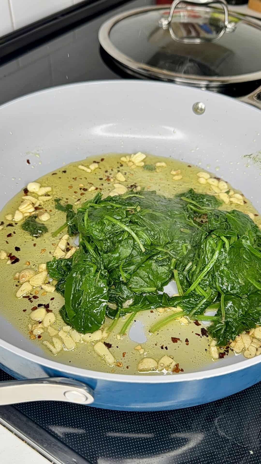 Spinach sautéing in a pan with garlic and red pepper flakes in oil.