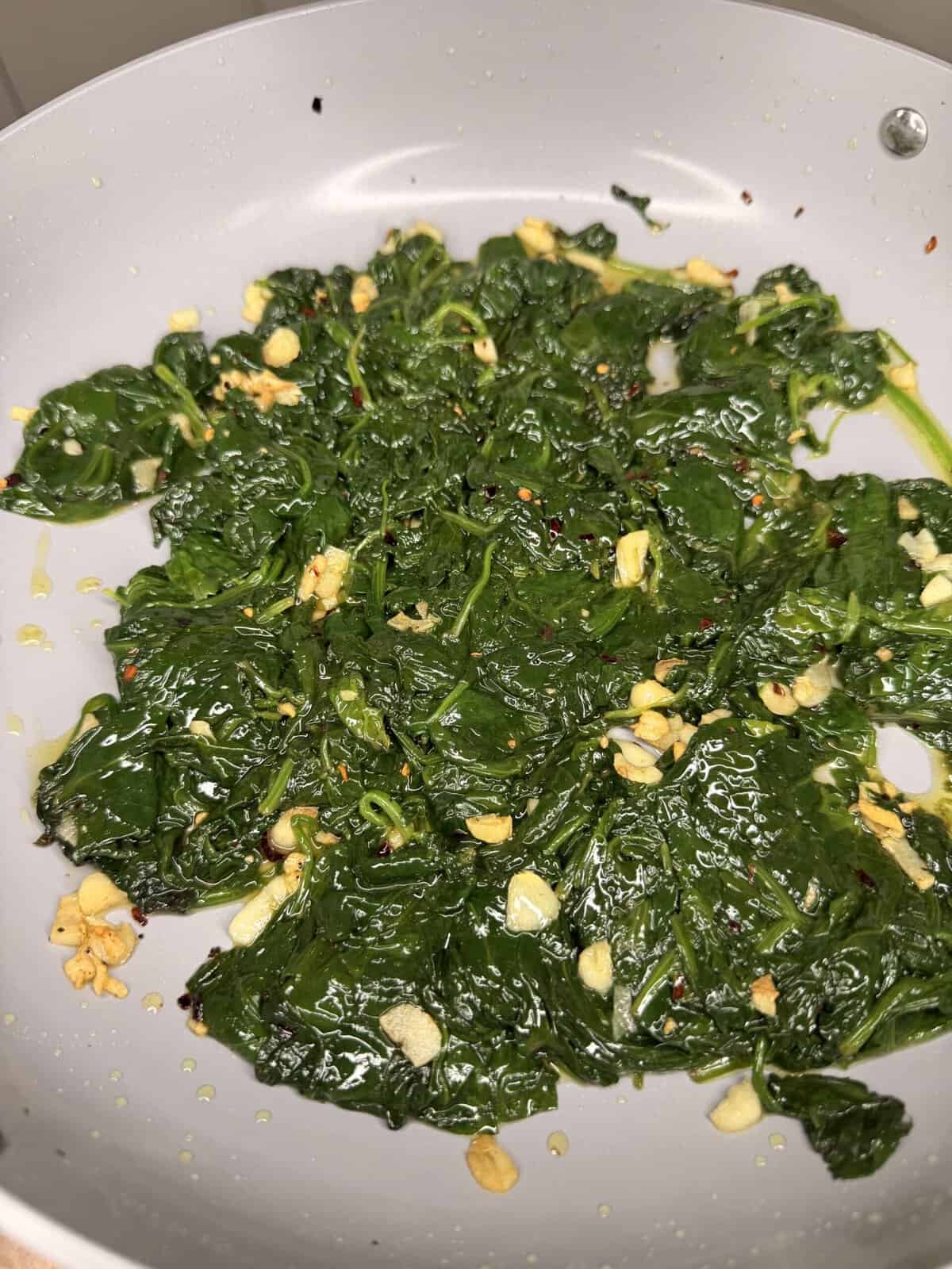Sautéed spinach with minced garlic and red pepper flakes in a light-colored pan.