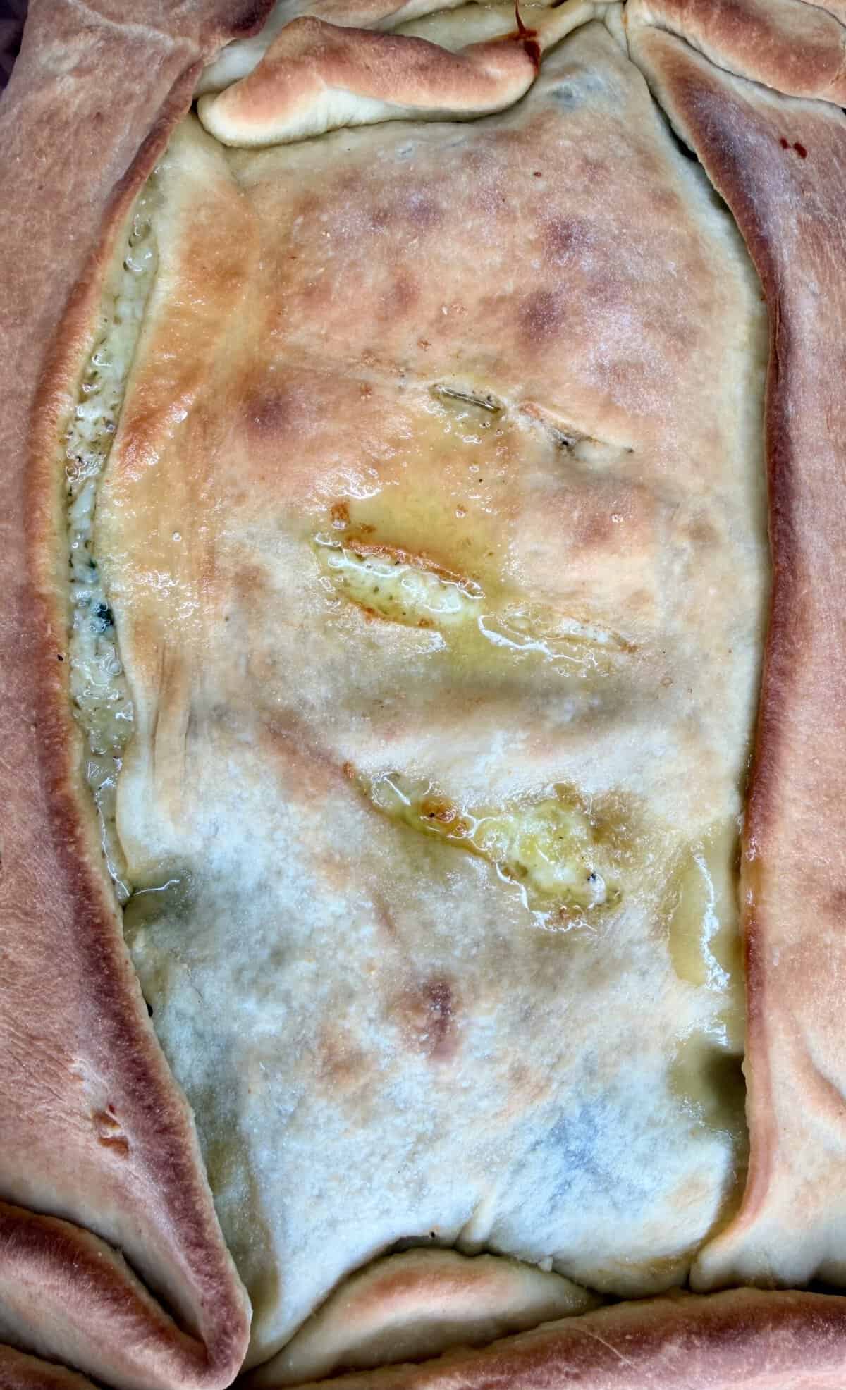 Close-up of a baked savory pie with a golden-brown crust and visible filling peeking through slits in the dough.