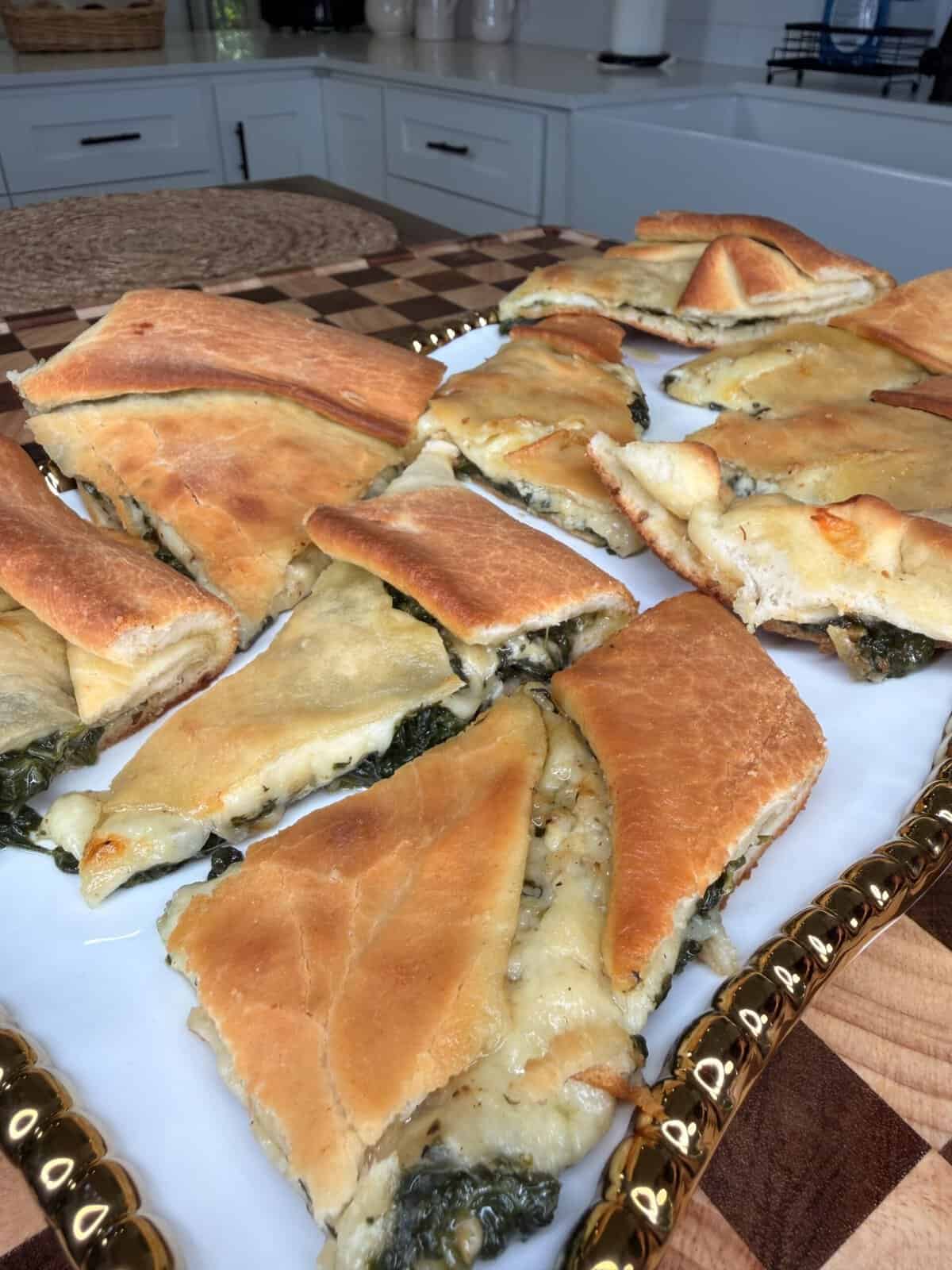 Slices of spinach and cheese flatbread arranged on a gold-rimmed white platter.