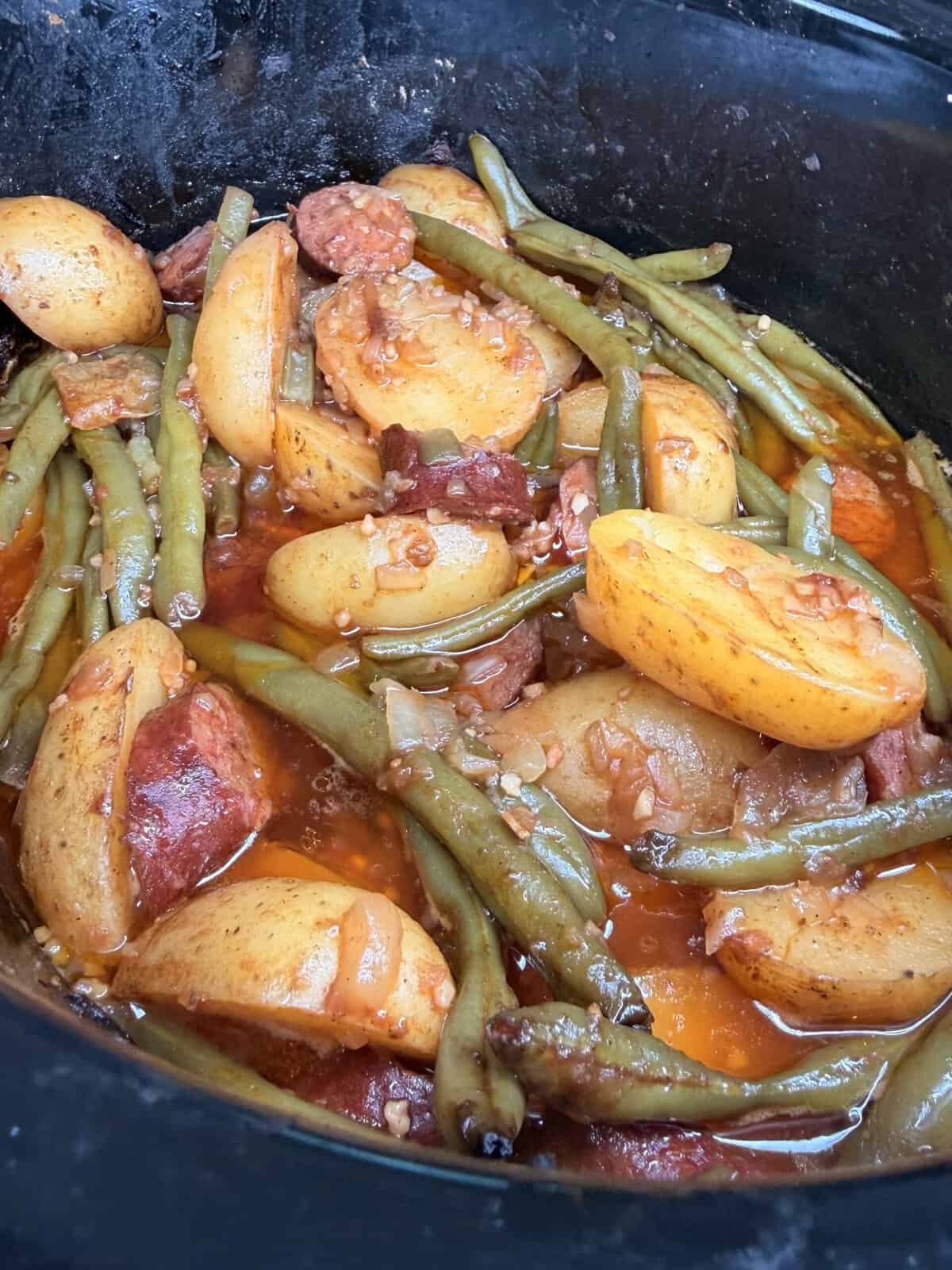 Slow cooker meal of sliced potatoes, green beans, and sausage in a savory broth.